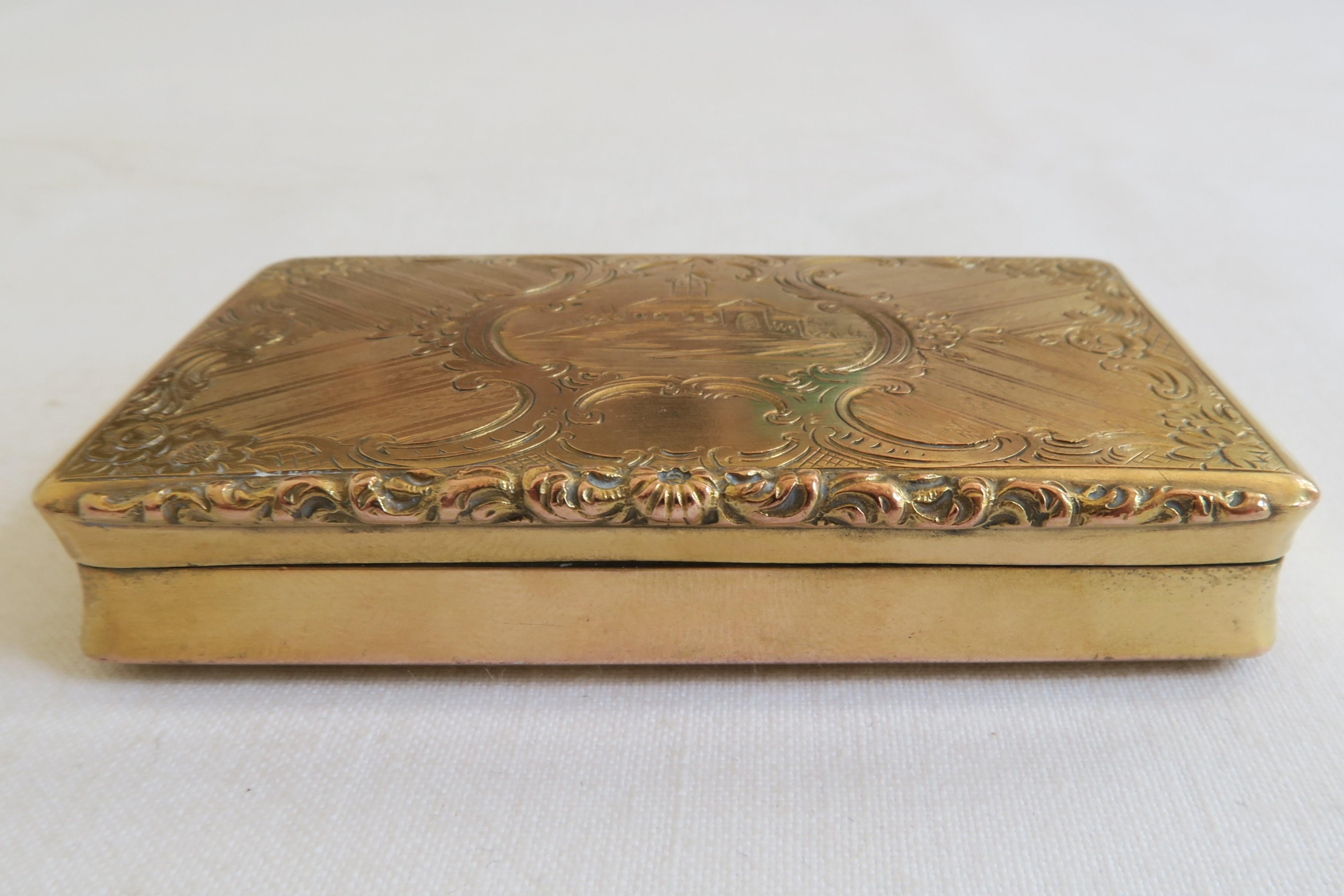 This beautiful snuff box is made from gold-plated sterling silver. The lid is embellished with a nice little graphic of a church surrounded by generous floral motives and ornament. Its bottom is a little more humble, covered in a graphic pattern.