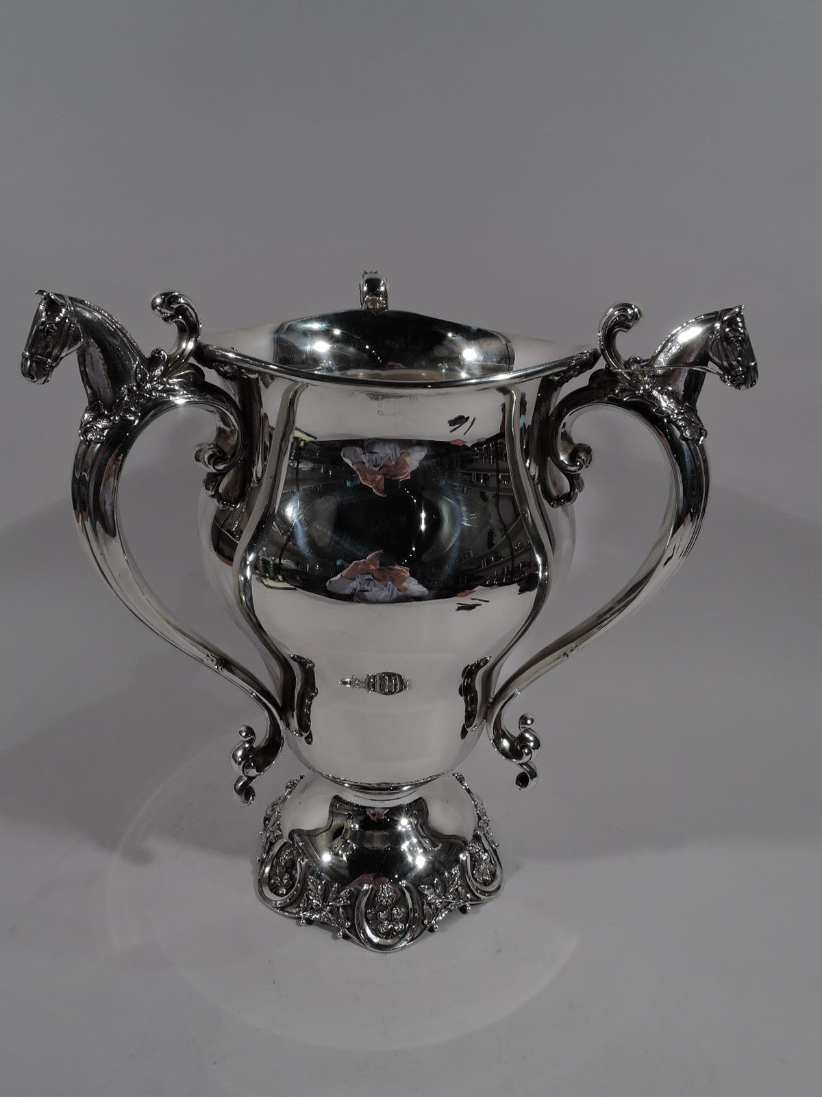 Turn-of-the-century American sterling silver loving cup trophy. Baluster with three scroll handles, each capped with cast horse bust encircled with wreath. Domed foot applied with leafing berry branches alternating with flowers set in horseshoes. On