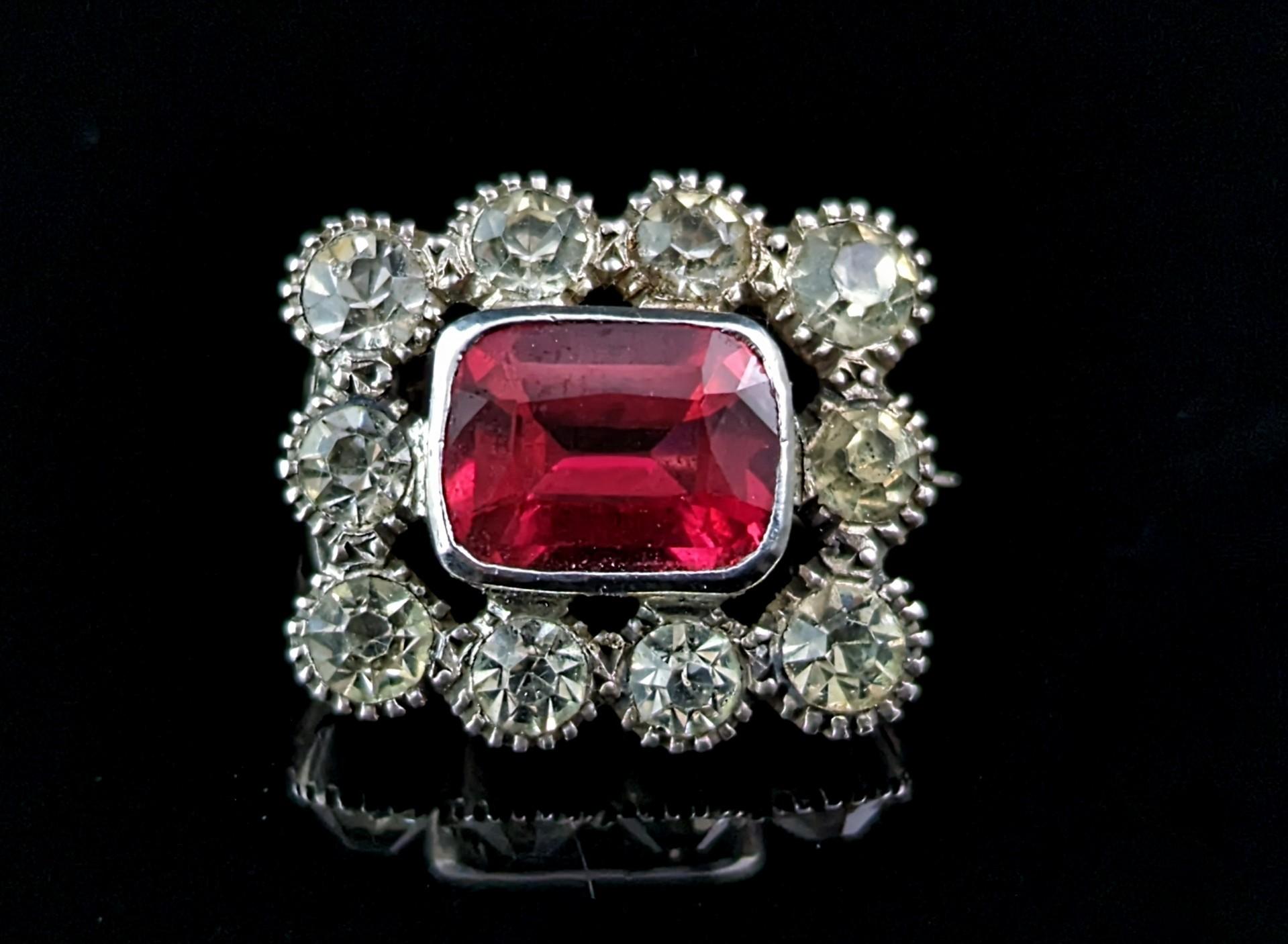 A sweet little antique sterling silver and paste lace pin or brooch.

It is crafted in sterling silver with a halo of clear paste stones surrounding a faceted emerald cut red paste stone.

Due to it's small size it was most probably a lace pin, used