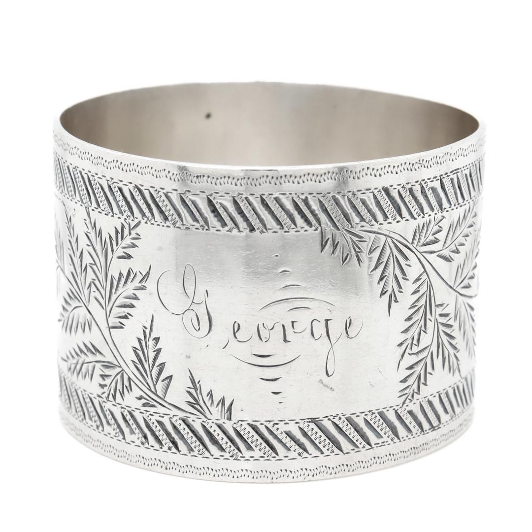 A fine antique napkin ring.

In sterling silver.

With engraved geometric and leaf garland decoration framing a central panel with the name 