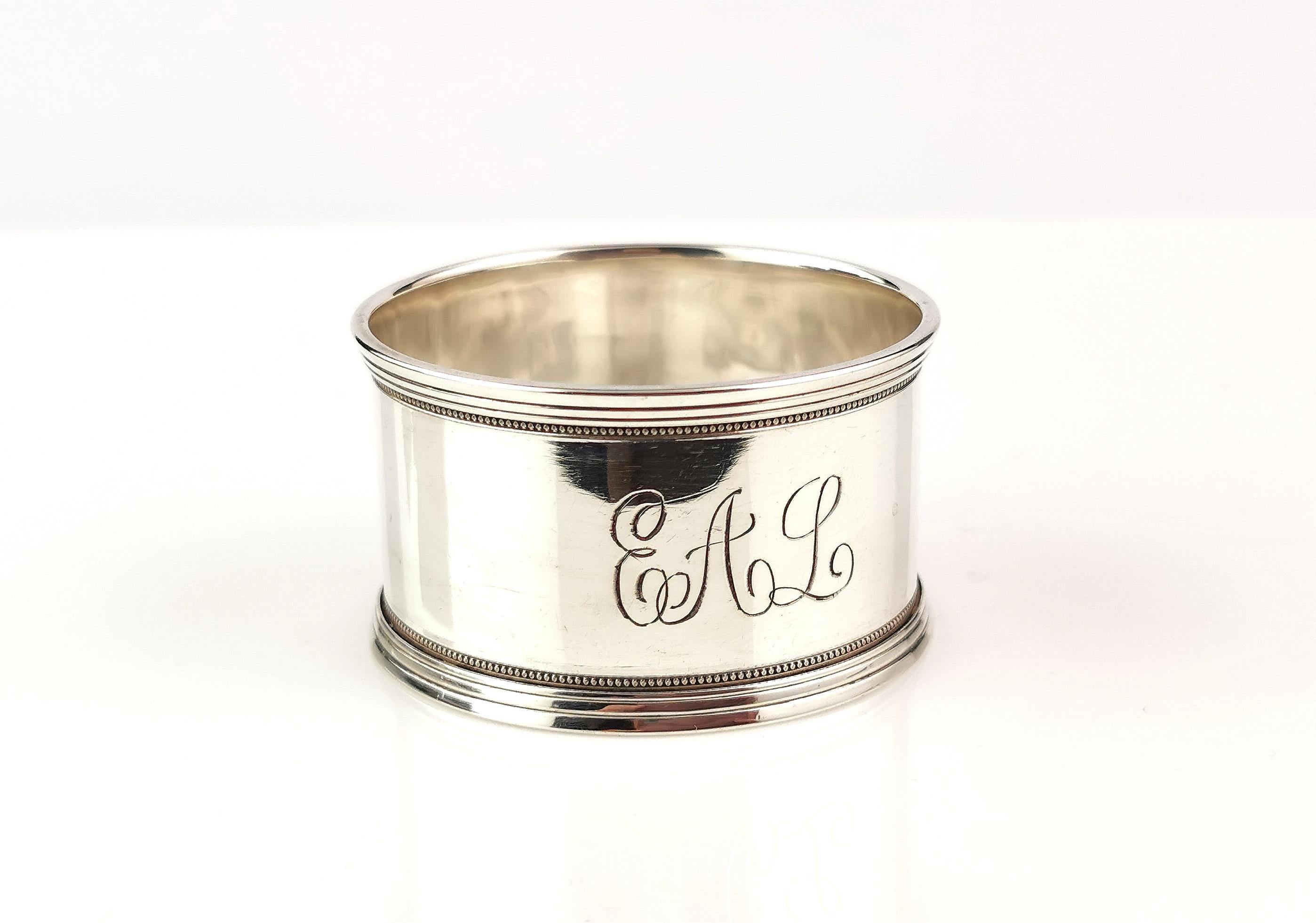 An attractive antique sterling silver napkin ring.

It is a sleek high polished napkin ring.

The body is a cylindrical shape with a slight rim that has a detailed millegrain edging top and bottom.

The monogram to the front has been hand engraved