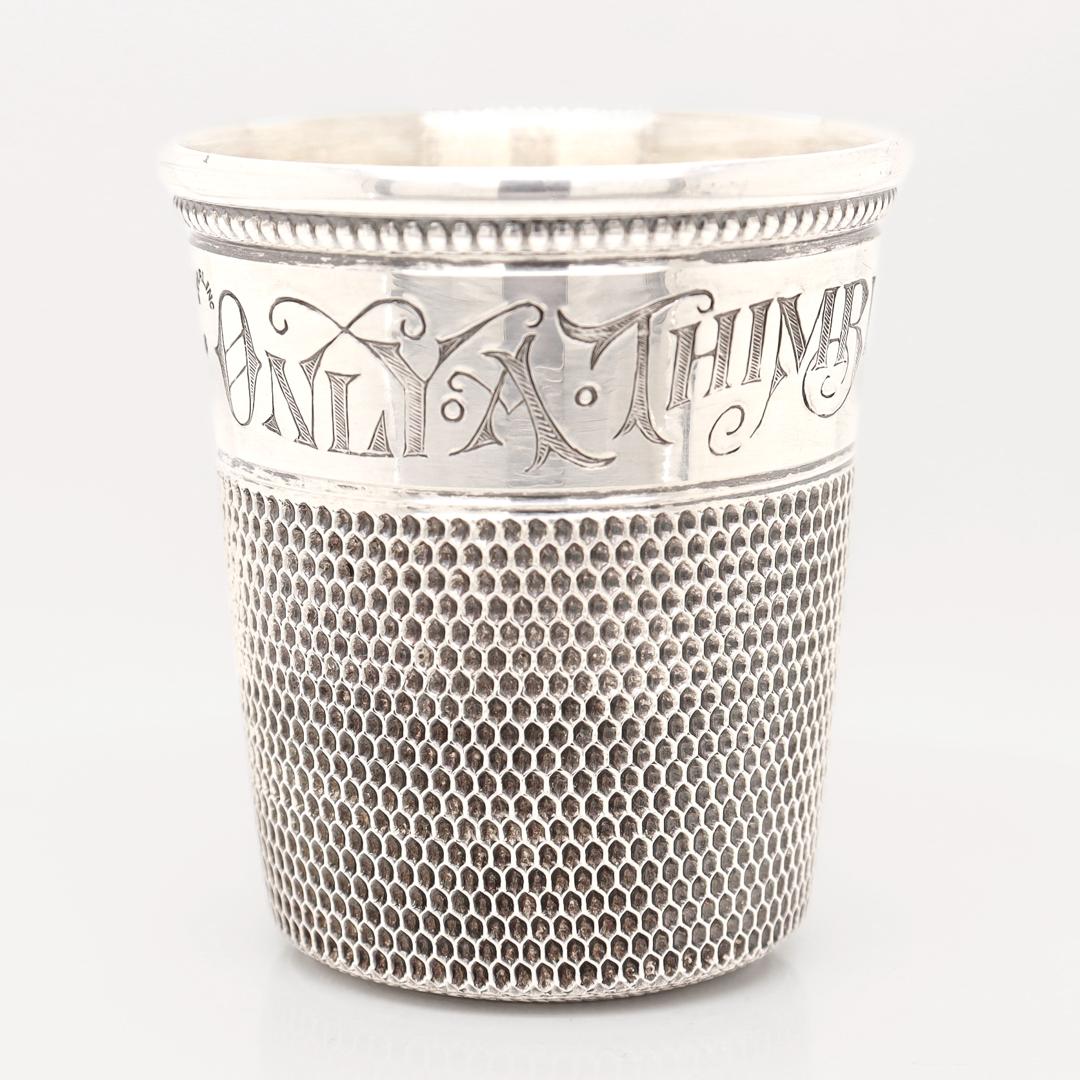 Un buen vaso de chupito o jigger antiguo.

En plata de ley.

En forma de dedal de coser de gran tamaño.

Grabado alrededor del borde 