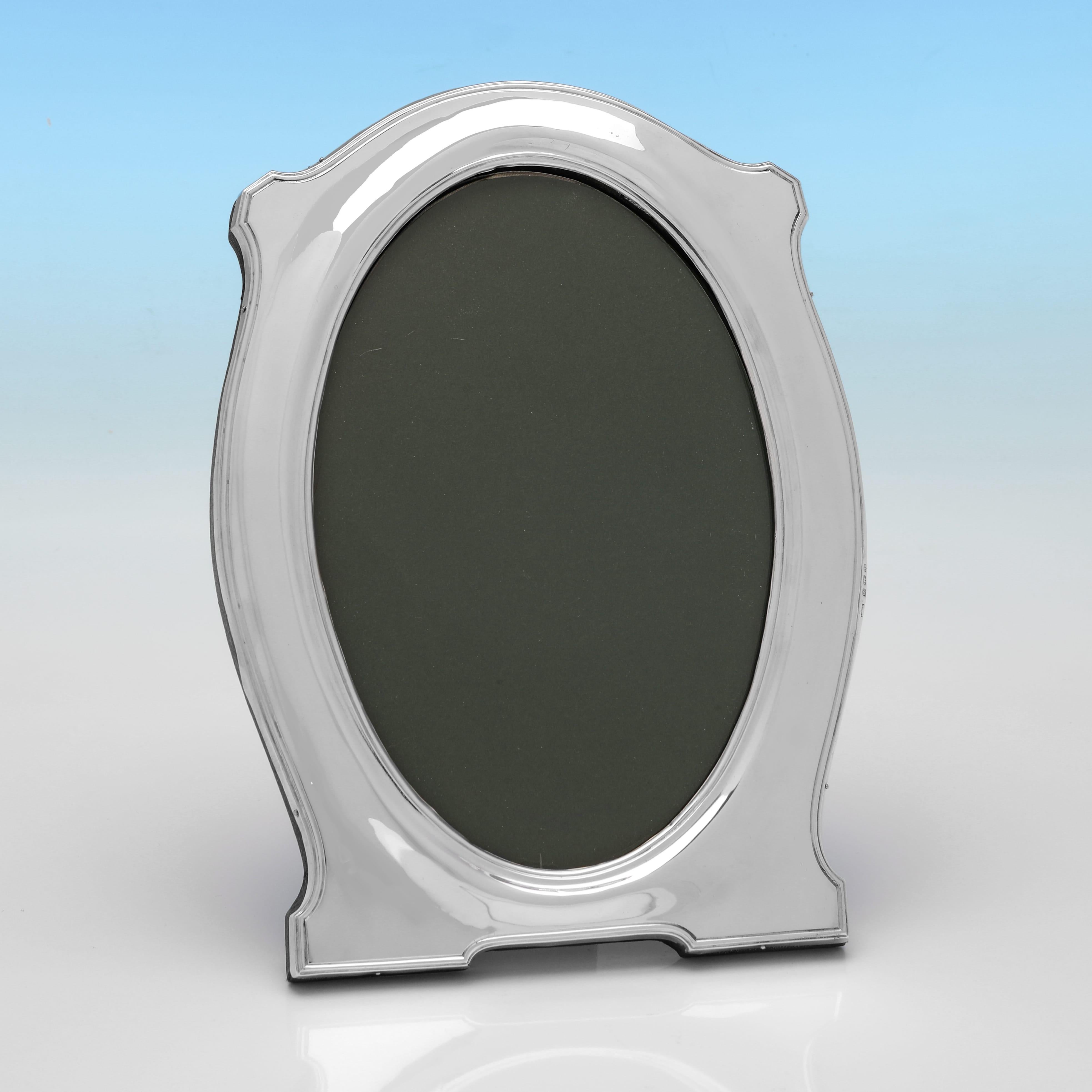Hallmarked in Birmingham in 1916, this stylish antique sterling silver photograph frame was made by Henry Clifford Davis during the early years of the George V period. The oval aperture is set within a softly contoured rectangular border, edged with