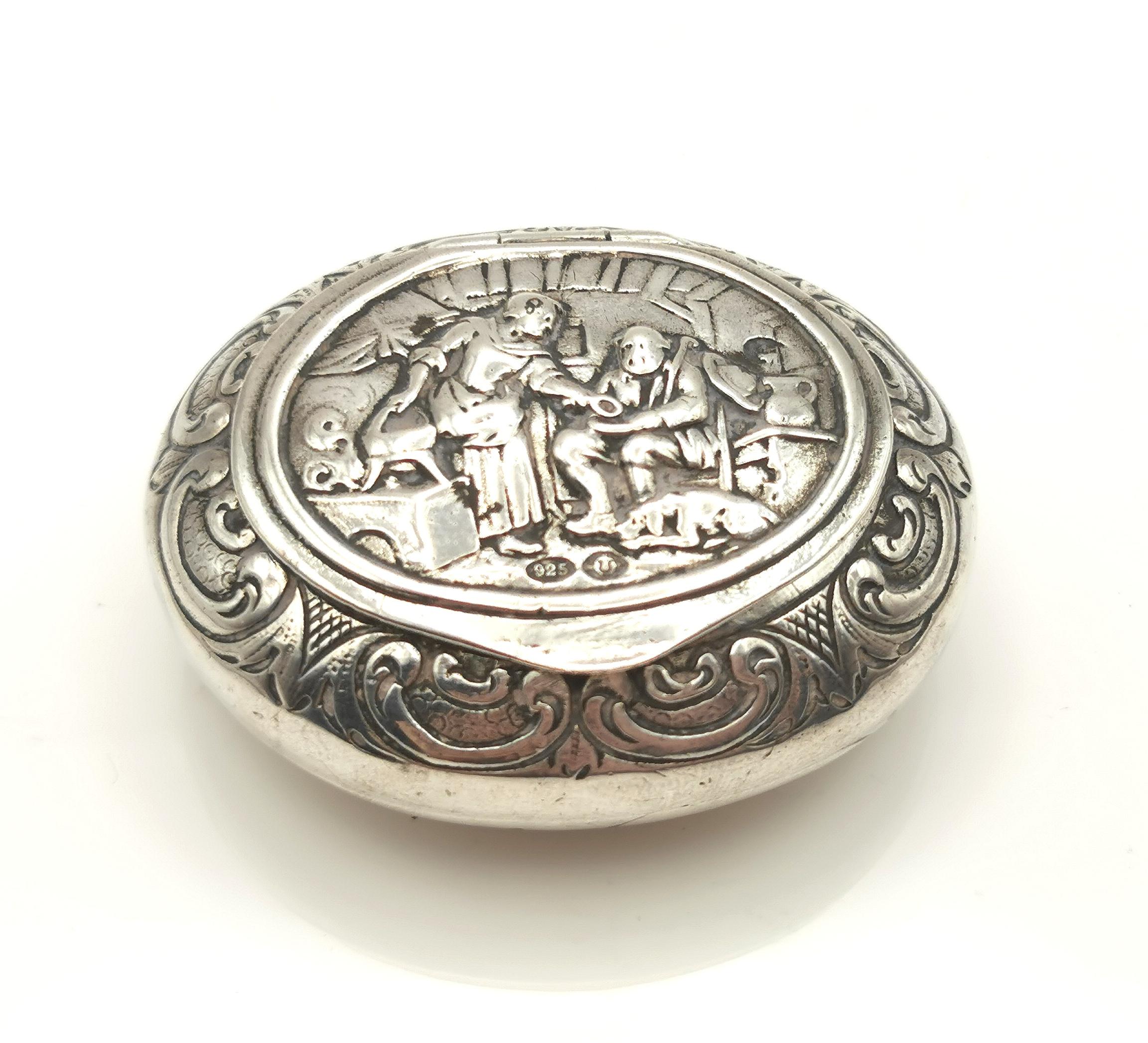 An attractive and decorative antique sterling silver snuff box.

It is a rounded oval shape, very ergonomic to slip into the pocket and it has a wonderful pictorial design to the lid in relief.

The scene is a home scene and features a woman by the