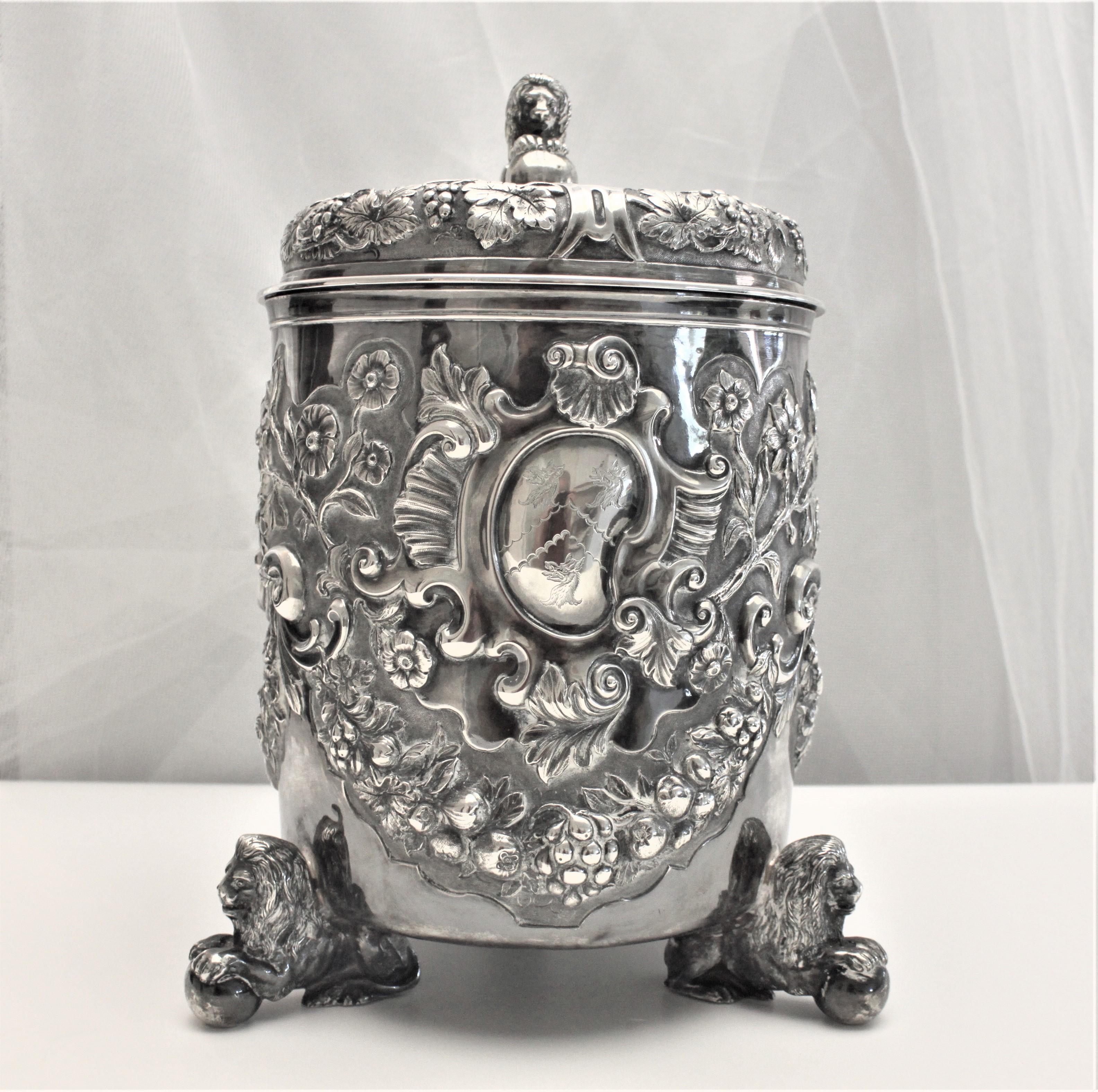 Esta sustanciosa cubitera con tapa estilo tankard está fabricada en plata de ley maciza y data de 1875, en la Inglaterra victoriana. La marca del fabricante está parcialmente oculta, pero hay la marca de servicio de la reina Victoria y las dos