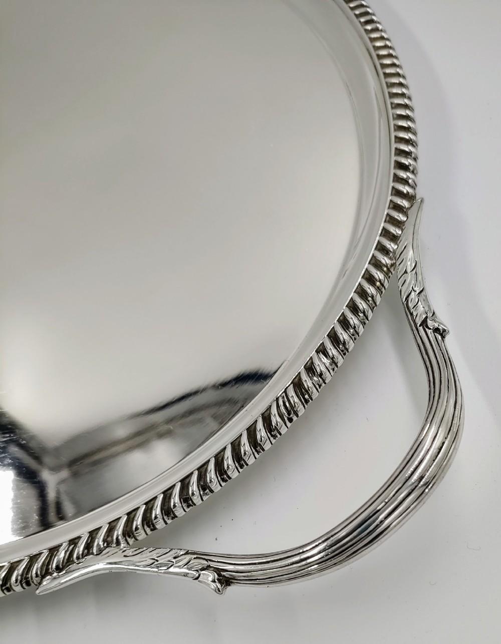 Item:- Antique sterling solid silver oval form tea tray. The surface of the tray is plain and unembellished. The tray has a raised curved border with heavy rope rim. Having two hooped reeded handles with acanthus leaf adornment. A must for any