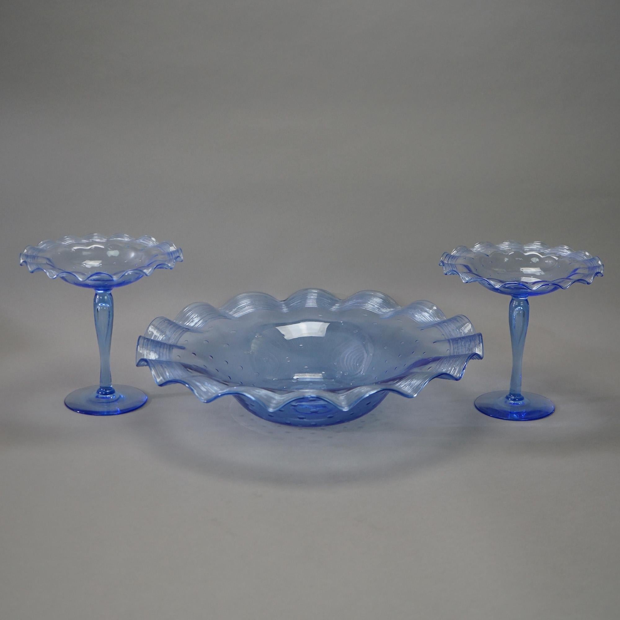 An antique garniture set by Steuben offers blue bubble art glass construction with ruffle rim center bowl and two stemmed compotes, unsigned, c1920

Measures- bowl 3.5''H x 15.5''W x 15.5''D; compotes 7''H x 7.5''W x 7.5''D.

Catalogue Note: Ask