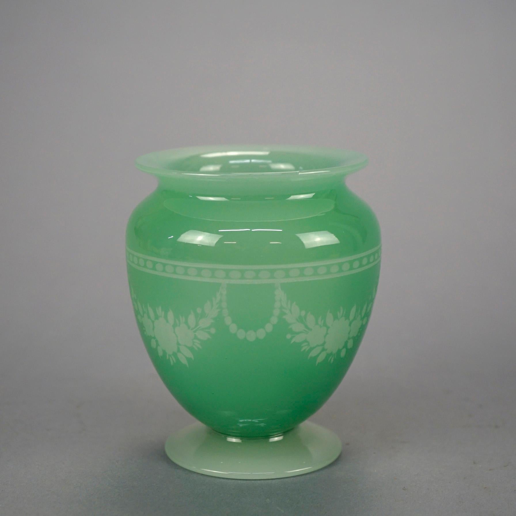An antique footed vase by Steuben offers green jade art glass construction with cut back floral swag design to alabaster, c1920

Measures- 5'' H x 4'' W x 4'' D.