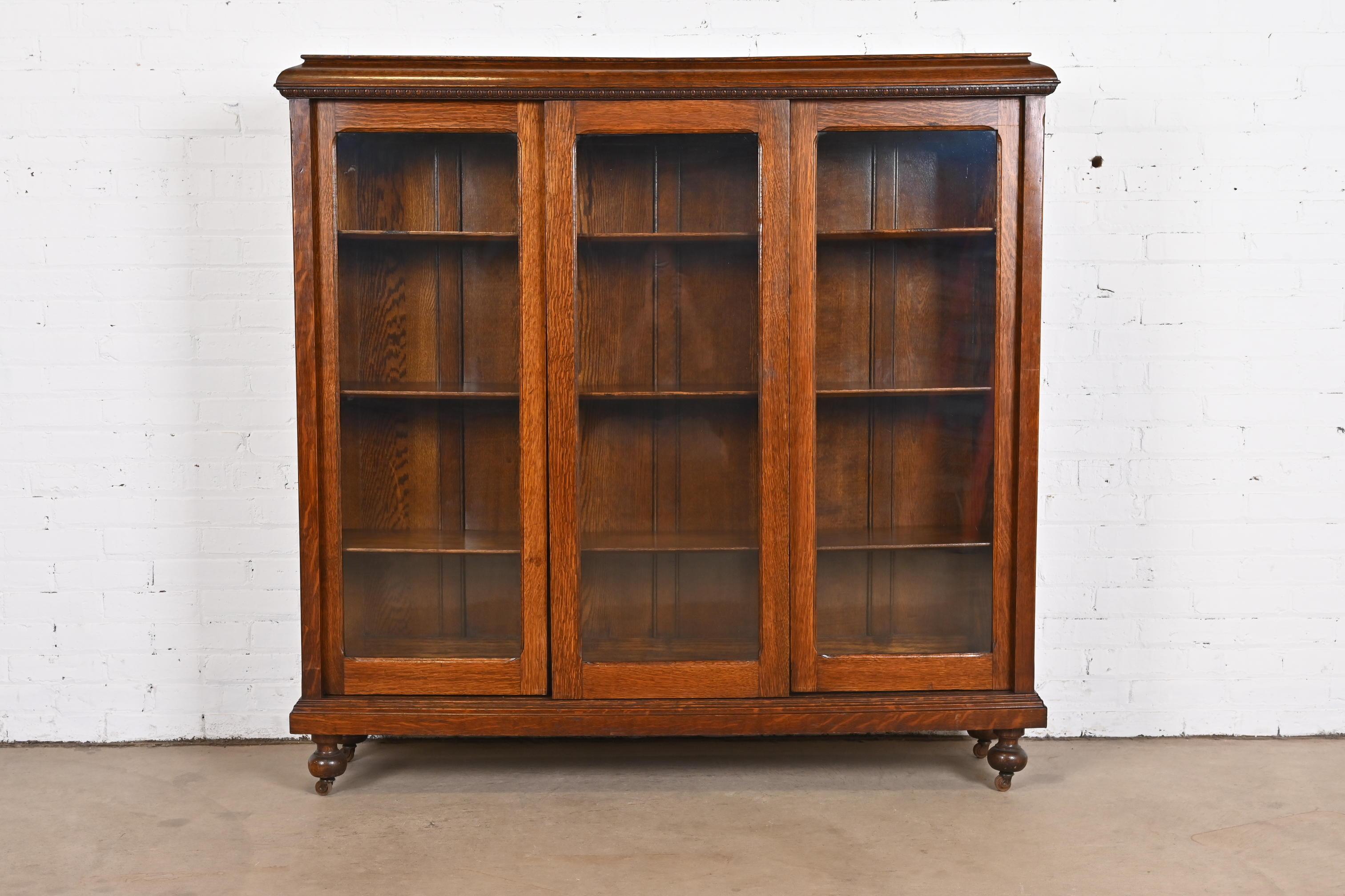 A beautiful antique Arts & Crafts triple bookcase cabinet

In the manner of Stickley

USA, circa 1900

Carved oak, with sliding glass front doors.

Measures: 57