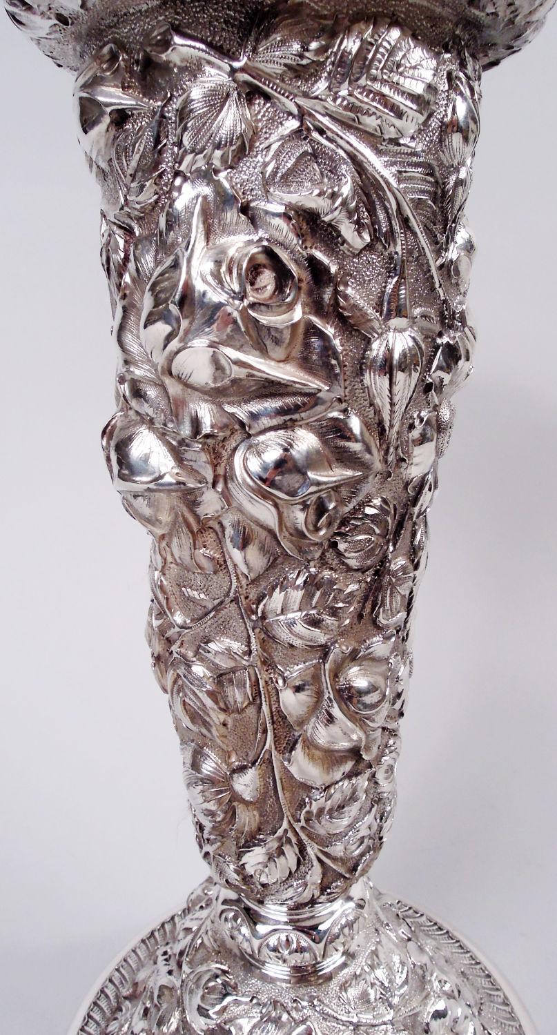 Vaso edoardiano in argento sterling. Realizzato da Stieff a Baltimora, circa 1925. Conico con anse superiori e inferiori; collo corto e bordo della bocca ondulato e piede a cupola. Densa repousse floreale su fondo punteggiato. L'esterno del collo ha