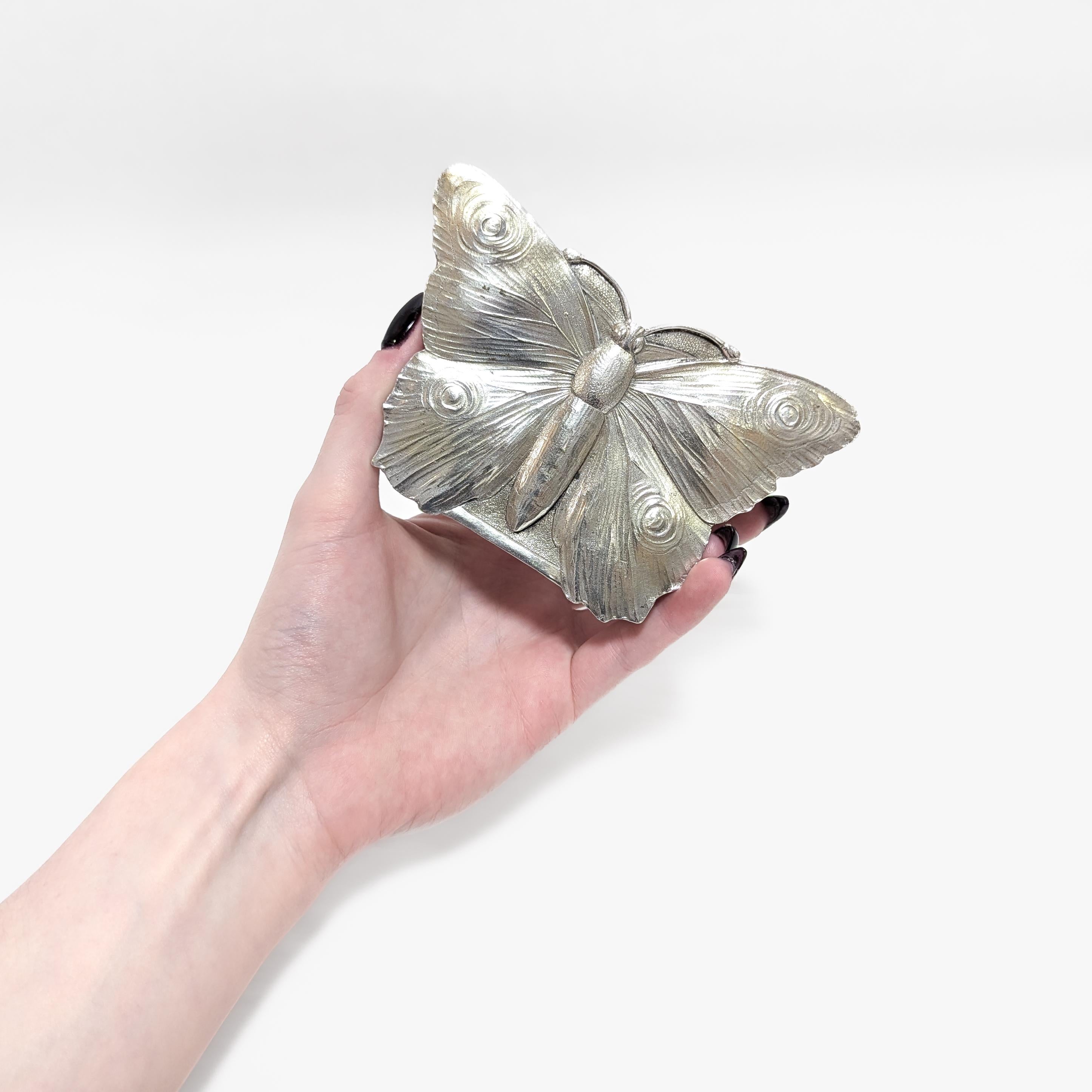In .800 silver.

By Storck & Sinsheimer of Hanau, Germany.

In the form of a butterfly with a strong resemblance to the European peacock butterfly. 

The sides of the box with repousse floral and acanthus leaf devices.

Gilt to the interior.

Fully