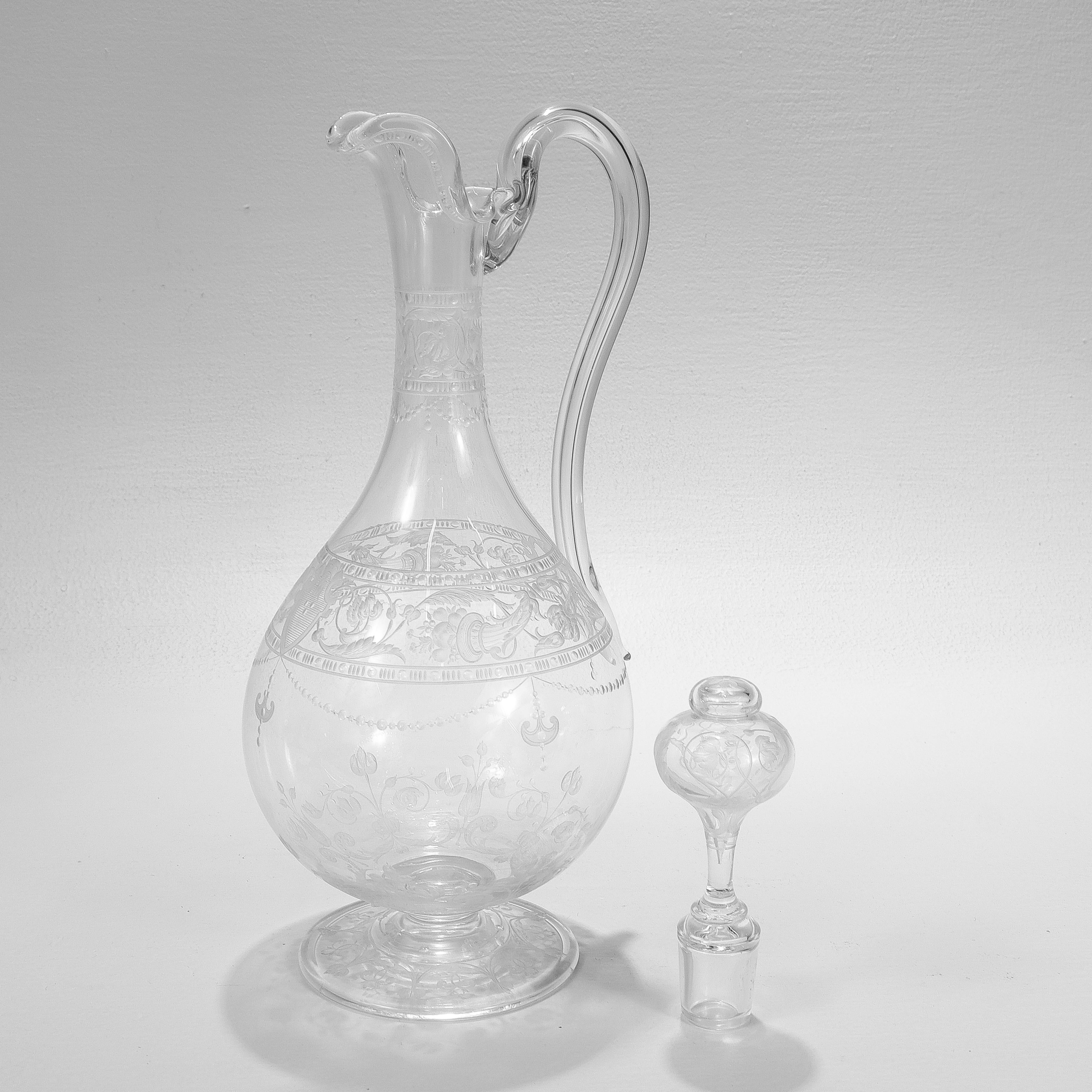 A fine antique English etched and engraved glass handled decanter.

Attributed to Stevens & Williams or Webb.

With engraved & etched designs trelliswork, flowers, and shield devices.

With a shaped rim, curved handle, and a stopper with cut leaf