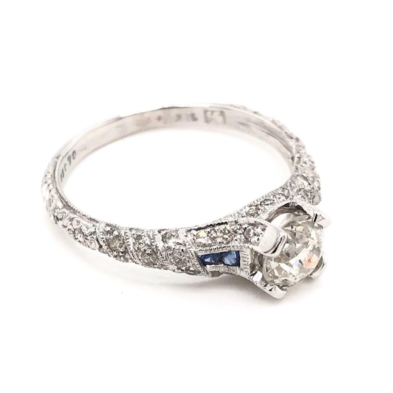 This diamond and sapphire ring is an estate piece. The setting is 18k white gold and features a 0.90 carat center diamond. The center Old European Cut diamond grades approximately J in color, SI1 in clarity. The white gold setting features 36