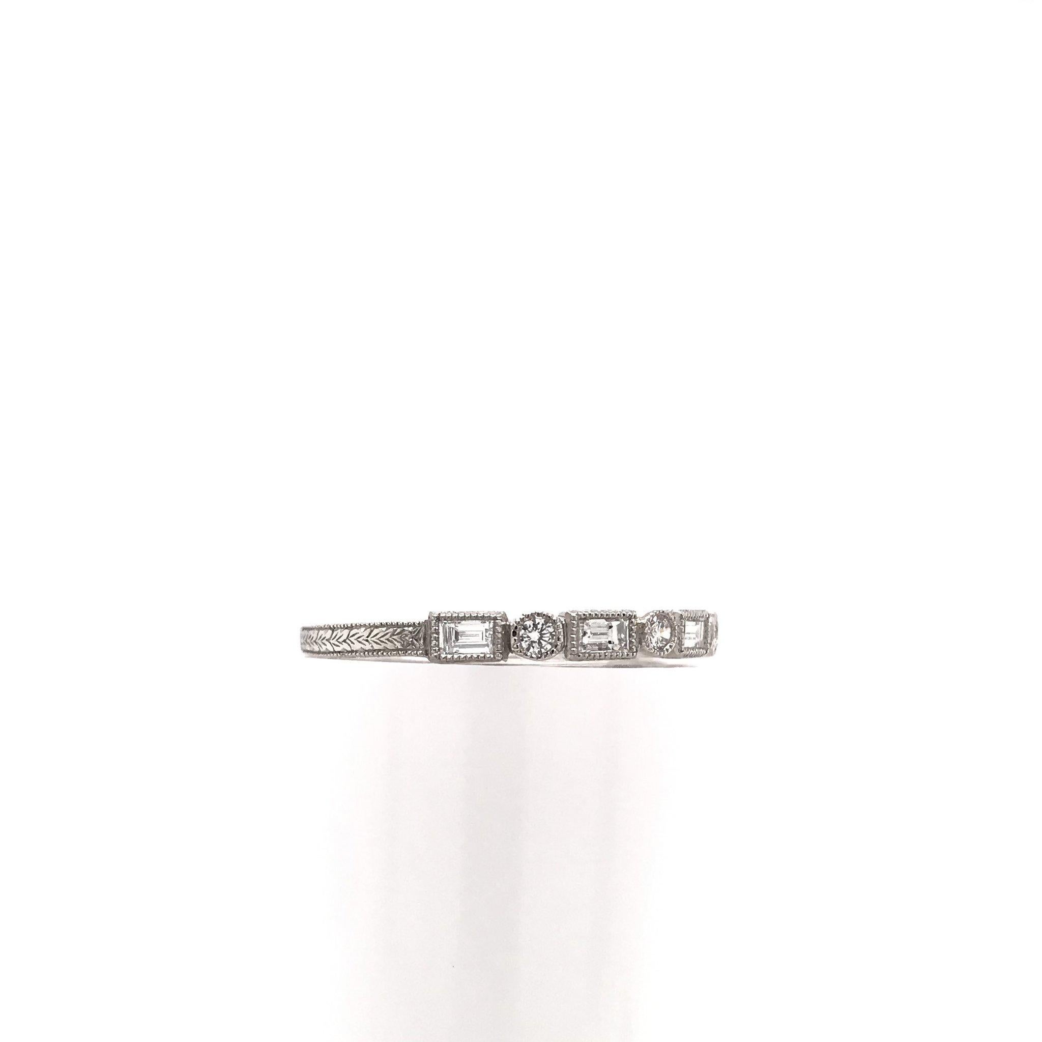 This piece is an extraordinary antique reproduction, meant to emulate the Art Deco design style. This platinum band features four sparkling round diamond accents as well as five baguette cut diamonds, extensive hand engravings, and fine milgrain