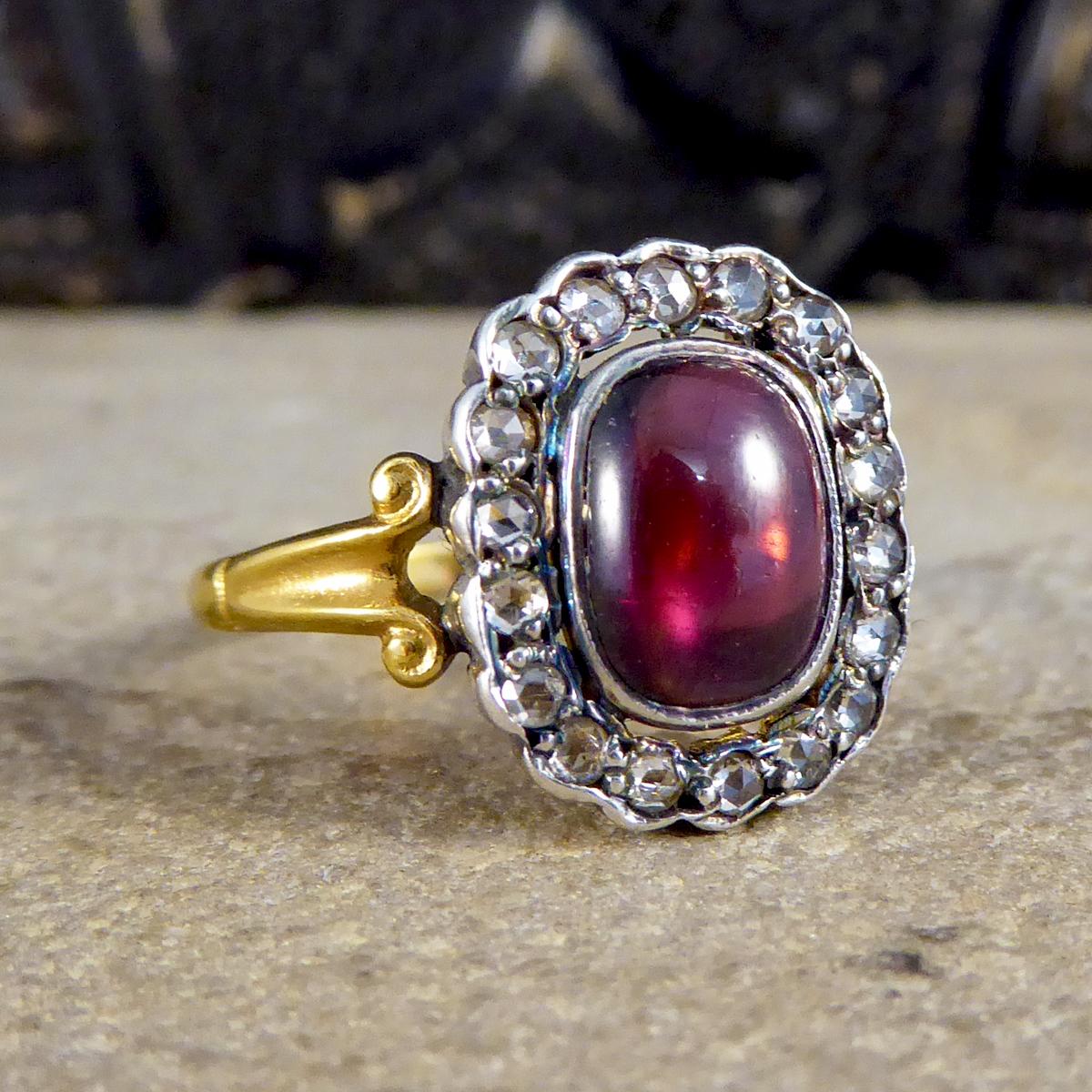 This beautiful contemporary ring has been crafted to resemble an antique style, it has an 18ct Yellow Gold band with scroll details on the shoulder leading to an 18ct White Gold setting holding a Cabochon Garnet stone in a rub over collar setting