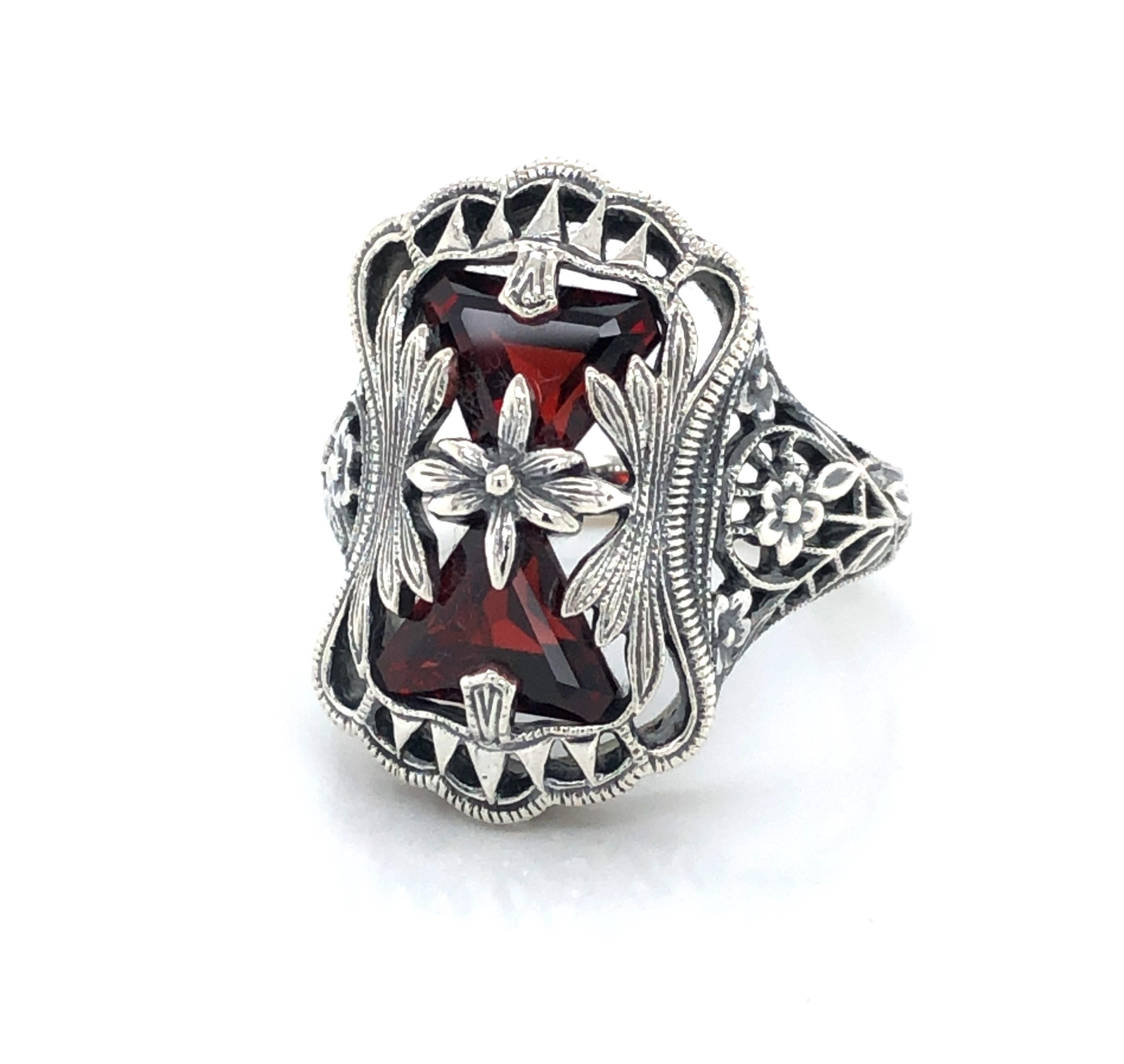 Two red garnet trillions, approximately one carat total weight, give this  beautiful antique inspired floral and vine sterling silver filigree ring it's rich look. The ornate ring head measures a generous 7/8 tall by approximately 1/2 inch wide.