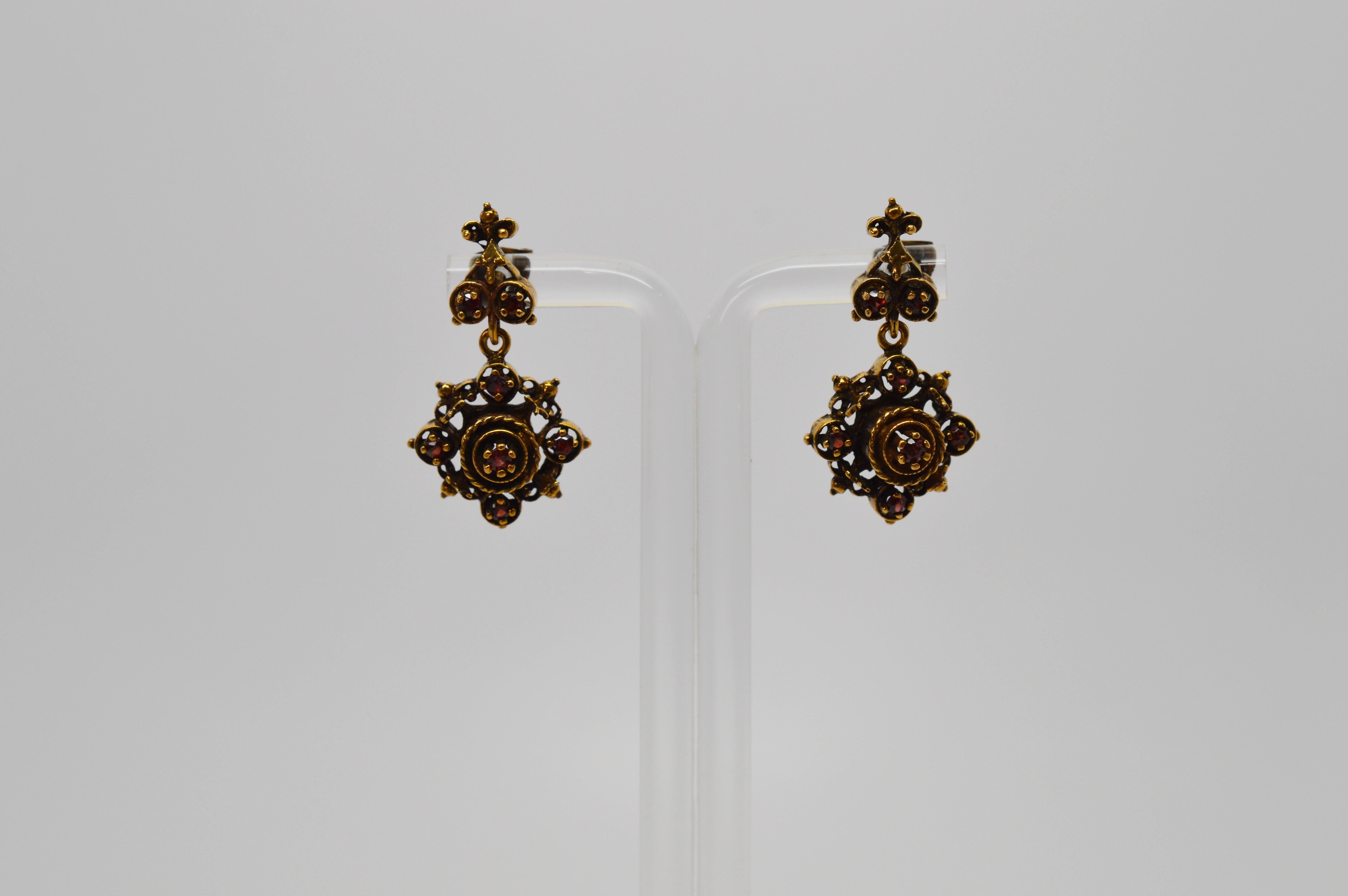 Rich deep red garnet gemstones accent this tastefully ornate pair of antique style fourteen karat (14k) yellow gold drop earrings. Secured by a decorative post , these medallion shaped gold earrings are for pieced ears, drop approximately 1-1/4 inch