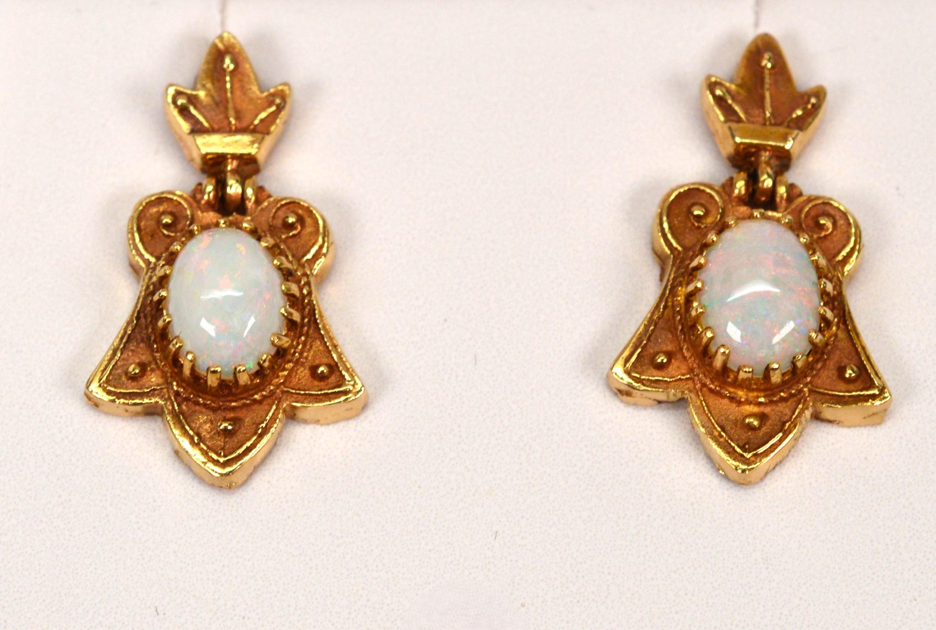Deux cabochons d'opale iridescents de 0,40 carat sont mis en valeur dans cette paire de boucles d'oreilles élégante mais modeste de style antique.
Fabriqués à la main en or jaune 14 carats, les médaillons ornés d'inspiration florale accueillent