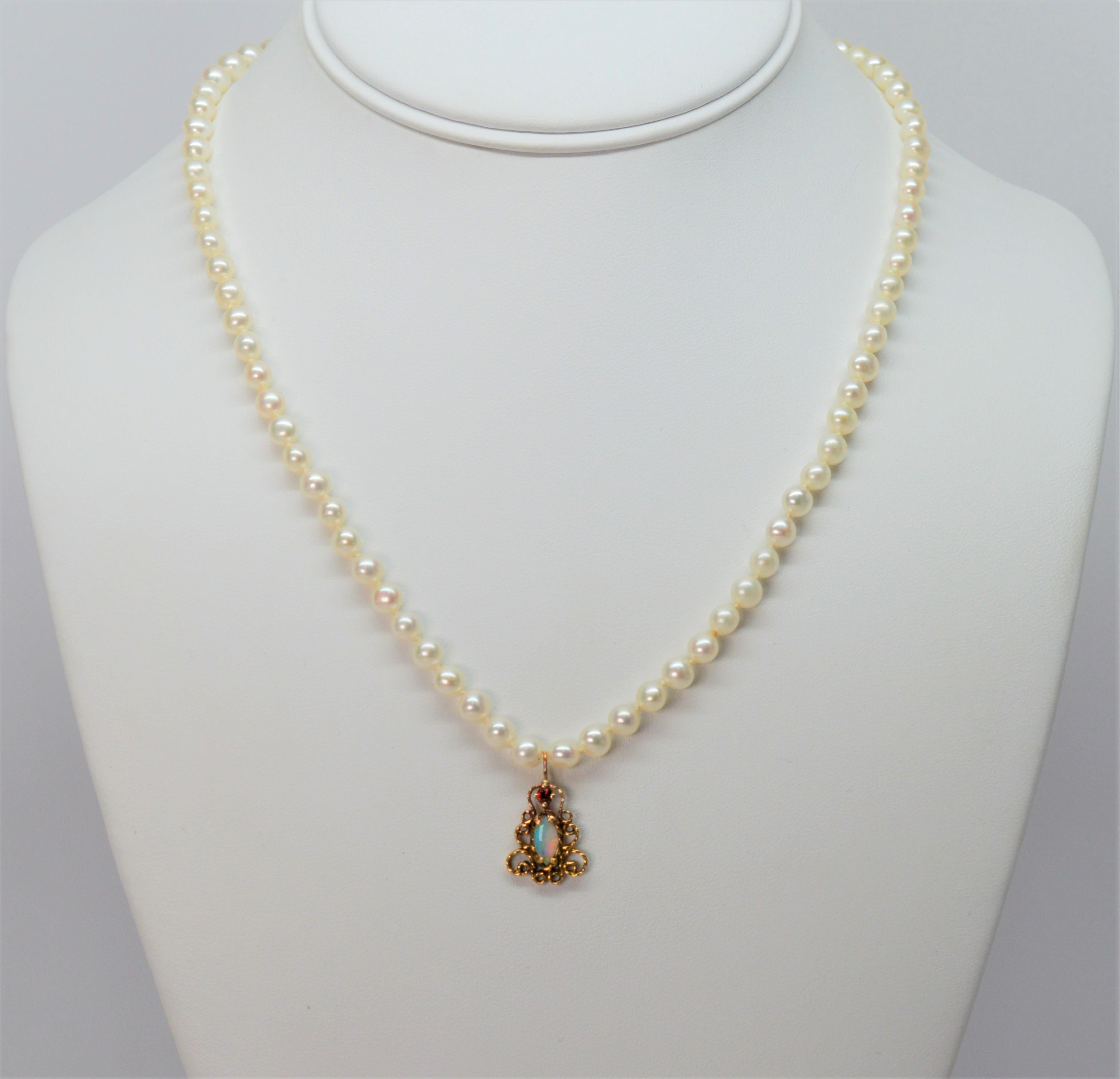 An eighteen inch strand of freshwater 5mm pearls leads to a dainty antique-style 14 karat yellow 3/4 inch gold charm pendant featuring an iridescent opal stone crowned with a petite red ruby. This darling necklace is finished with a 14 karat yellow