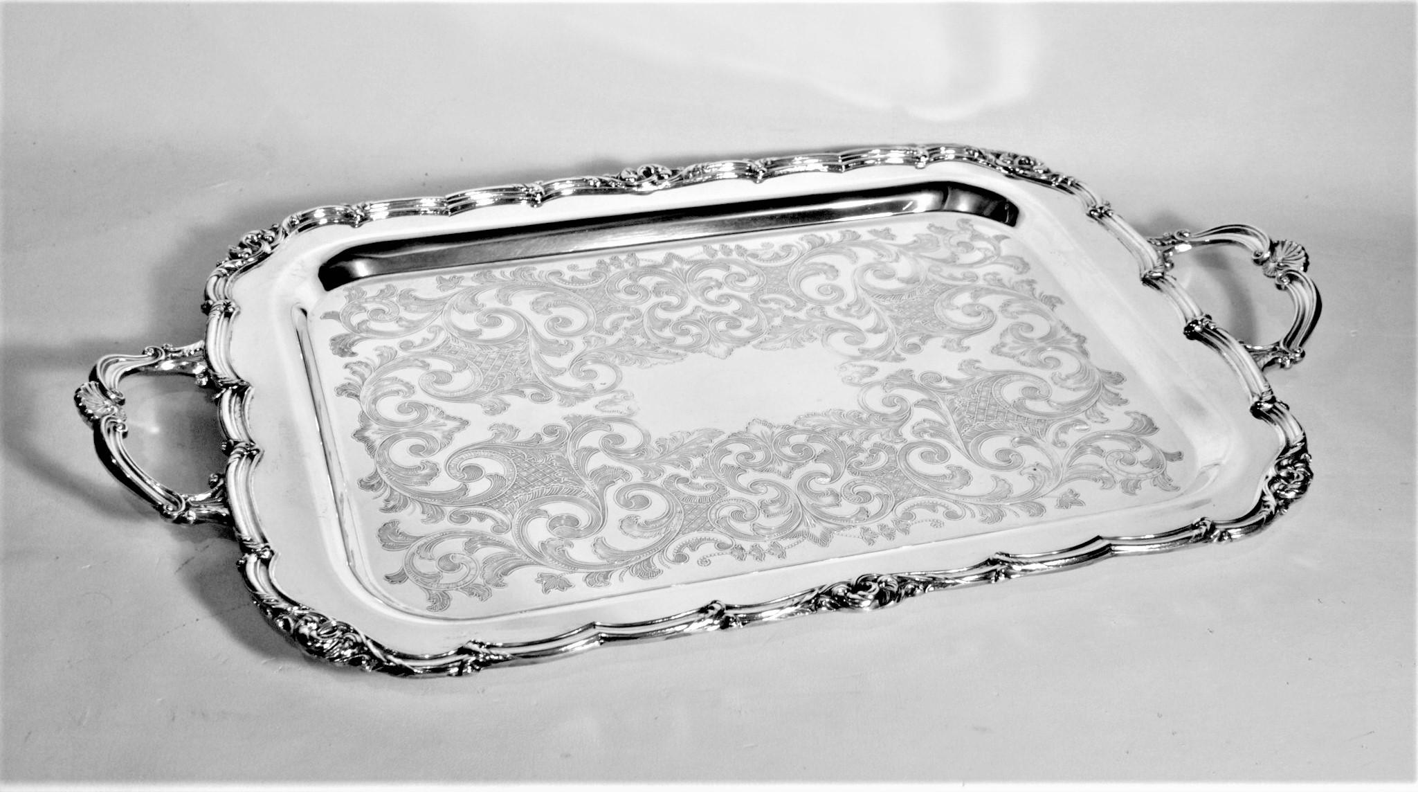 This small antique styled silver plated serving tray is hallmarked by an unknown maker, but originates from Canada from approximately 1950 in an English Victorian style. The rectangular shaped tray has a nicely scalloped outer rim with complimentary
