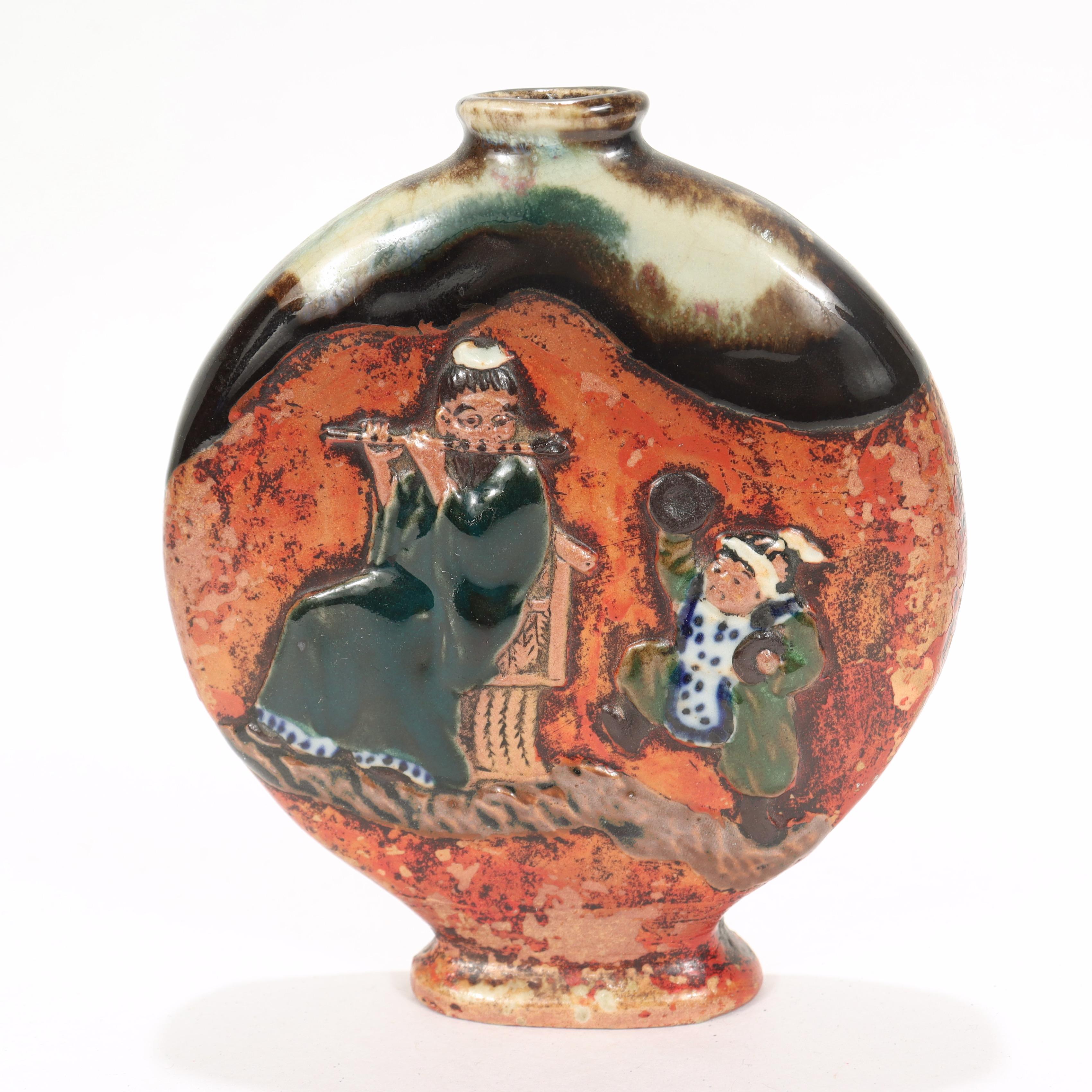 A fine antique Japanese Sumidagawa pottery moon flask vase.

Decorated to both sides. 

One side has a man playing a shinobue flute and a child dancing with a cymbal in each hand, while the other side depicts a lone sailboat in the ocean with