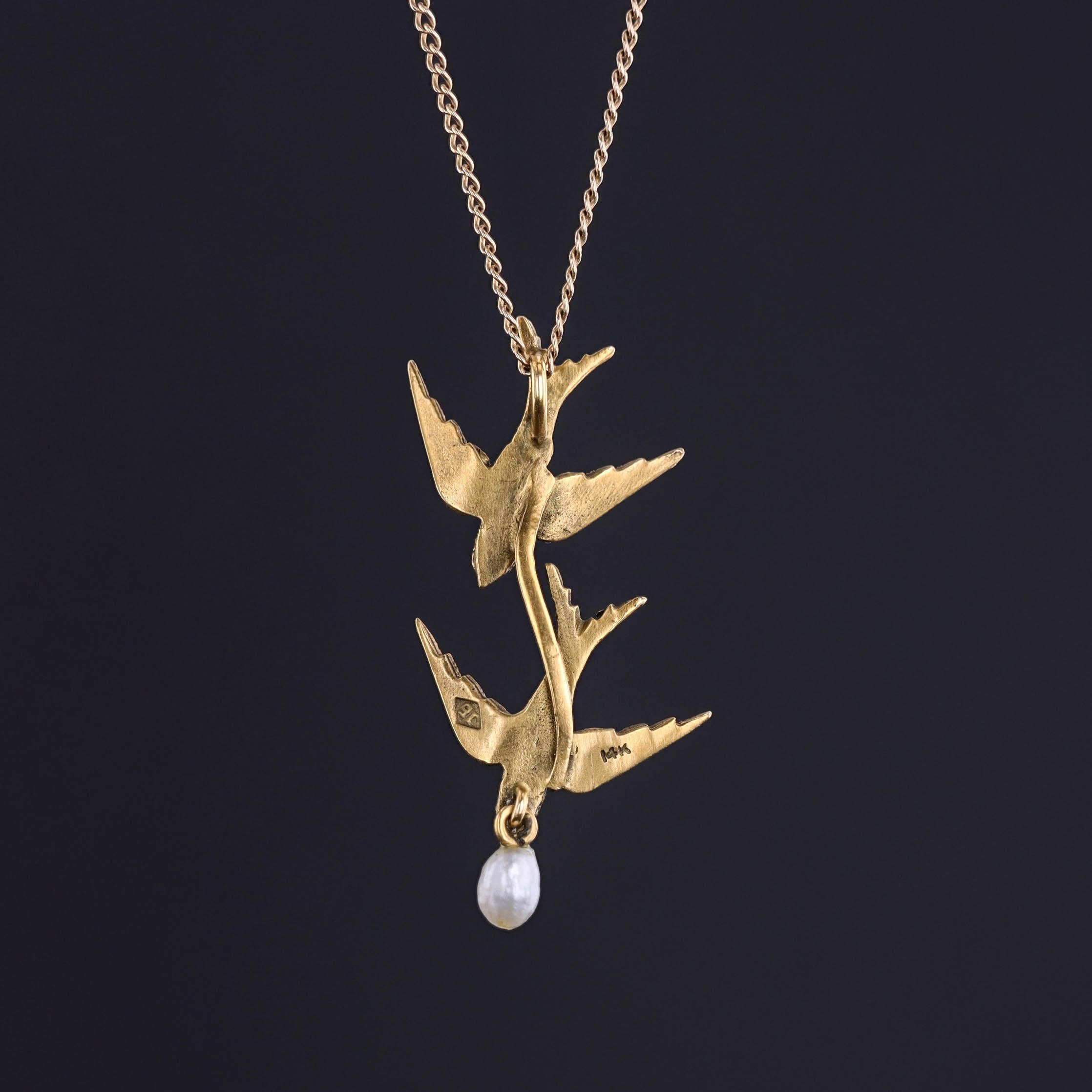 Grácil y simbólico, este encantador collar de golondrinas presenta dos golondrinas en vuelo, elaboradas en cálido oro de 14k, y acentuadas por una única y elegante perla colgante. Esta pieza, que originalmente era un broche de 1900, fue