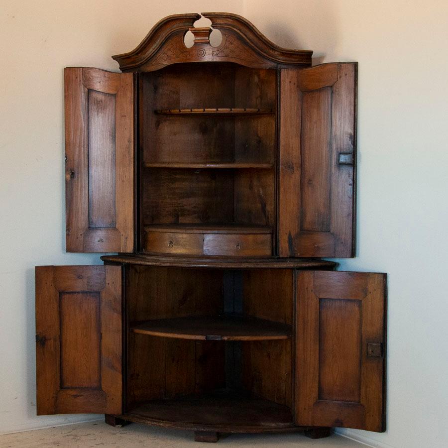 It is the deeply aged patina of the pine that one finds entrancing in this beautiful carved corner cabinet. Every detail reveals the touch of a talented craftsman, from the curved bonnet to lattice etched details inside each panel and the delicately