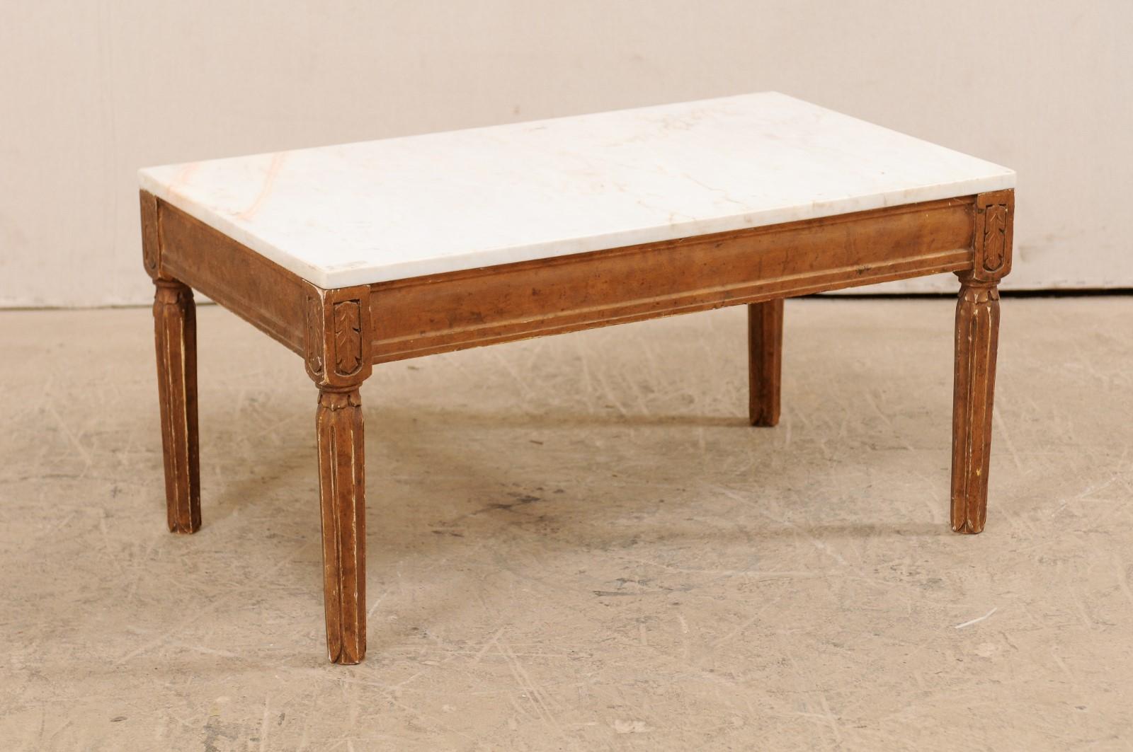 A Swedish coffee table with white marble top from the early 20th century. This antique table from Sweden features a rectangular-shaped white marble top which rests above a wood skirt, minimally adorn with straight trim and carved leaf accents at