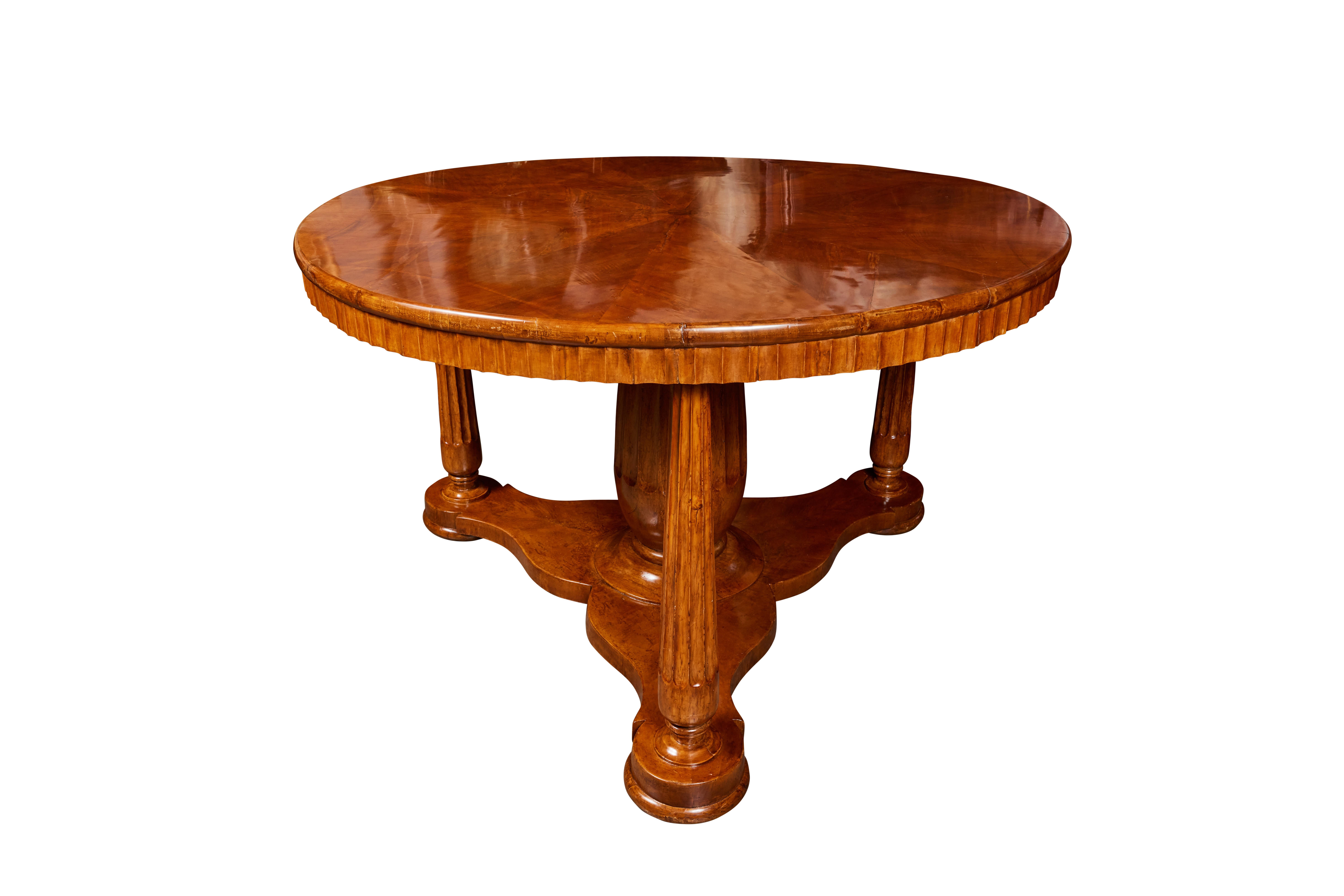 A beautiful, large, hand-carved walnut veneered center table on tapered, fluted legs above a unique, tri-petal base. The top surrounded by a matching, fluted edge.