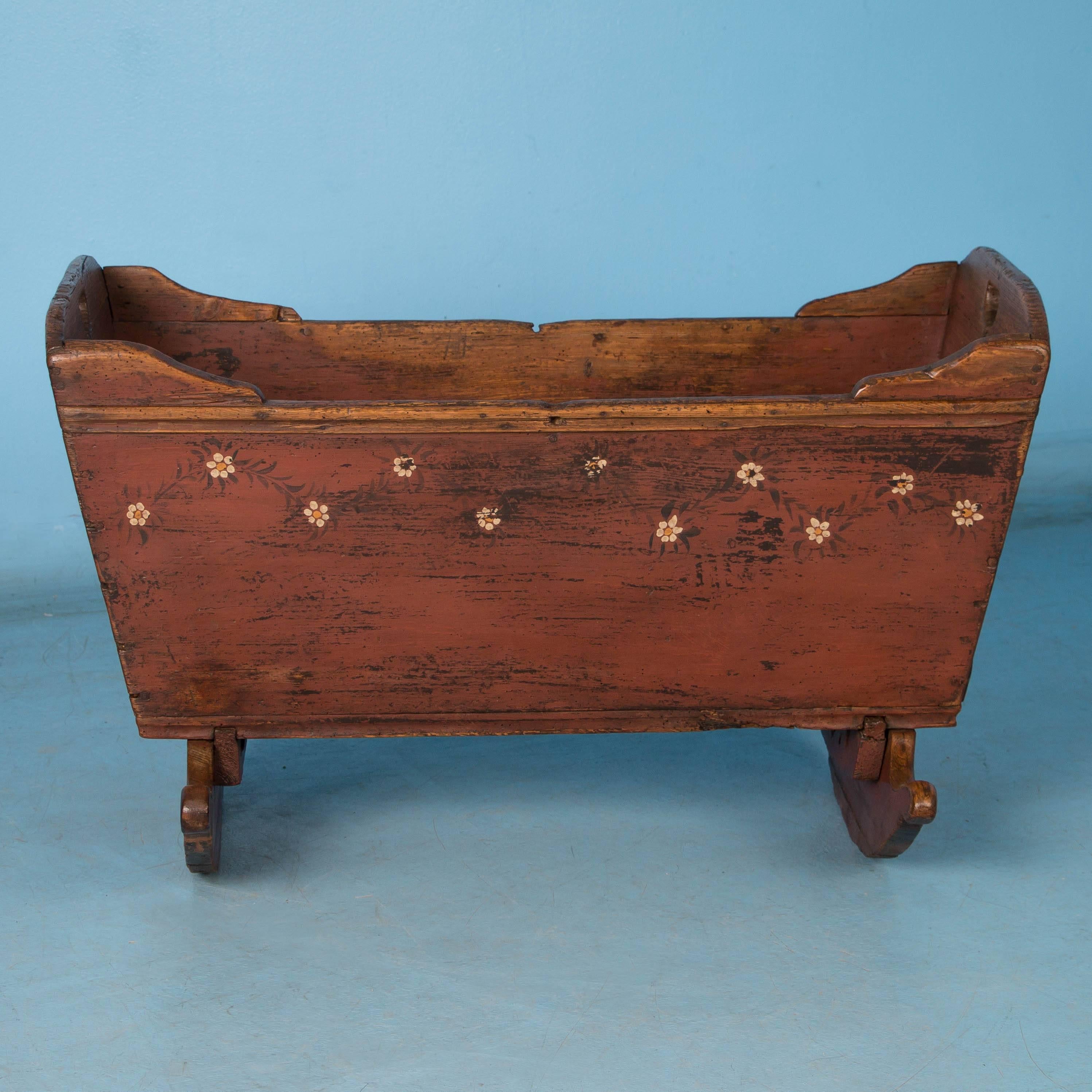 This charming 19th century cradle with the original warm, rust colored paint is visually outstanding. The white floral design, monogram and date of 1852 add to the Folk Art quality and most appealing is where the paint is worn away from years of use