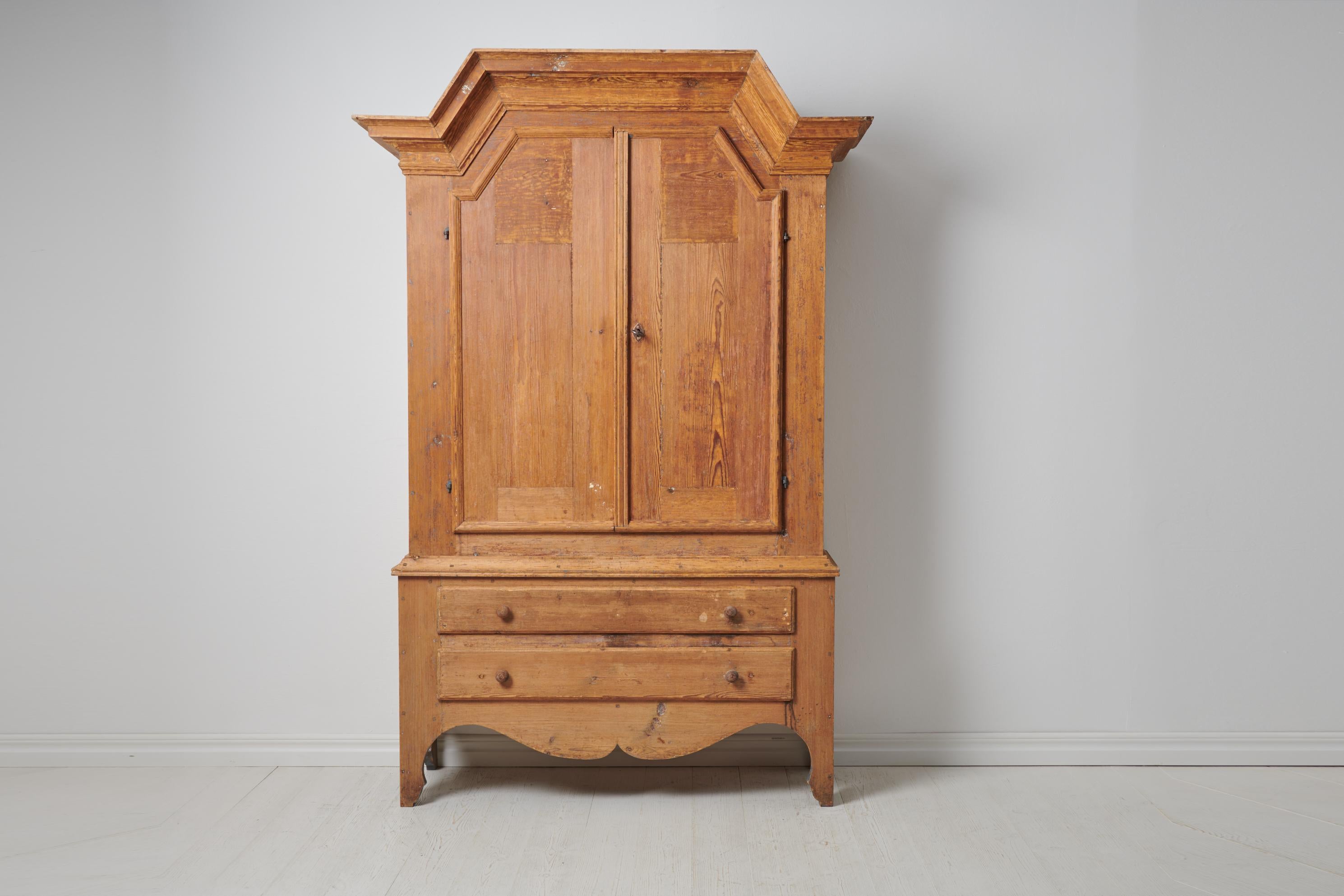 Antique folk art cabinet from Sweden made during the first years of the 19th century, around 1810. The cabinet is made by hand in solid pine. The cabinet has a rustic surface with bare pine wood where the grain of the wood is visible. The joints are