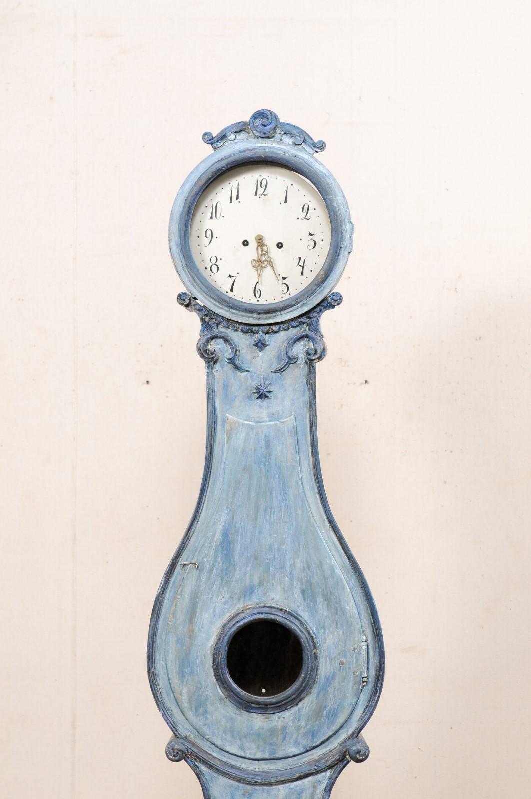 A Swedish Fryksdahl floor clock with shapely body and carved crown from the 19th century. This antique Fryksdahl clock from Sweden has a raised crest which is carved in swirling medallion at center, flanked within a pair of leafy scrolls, resting