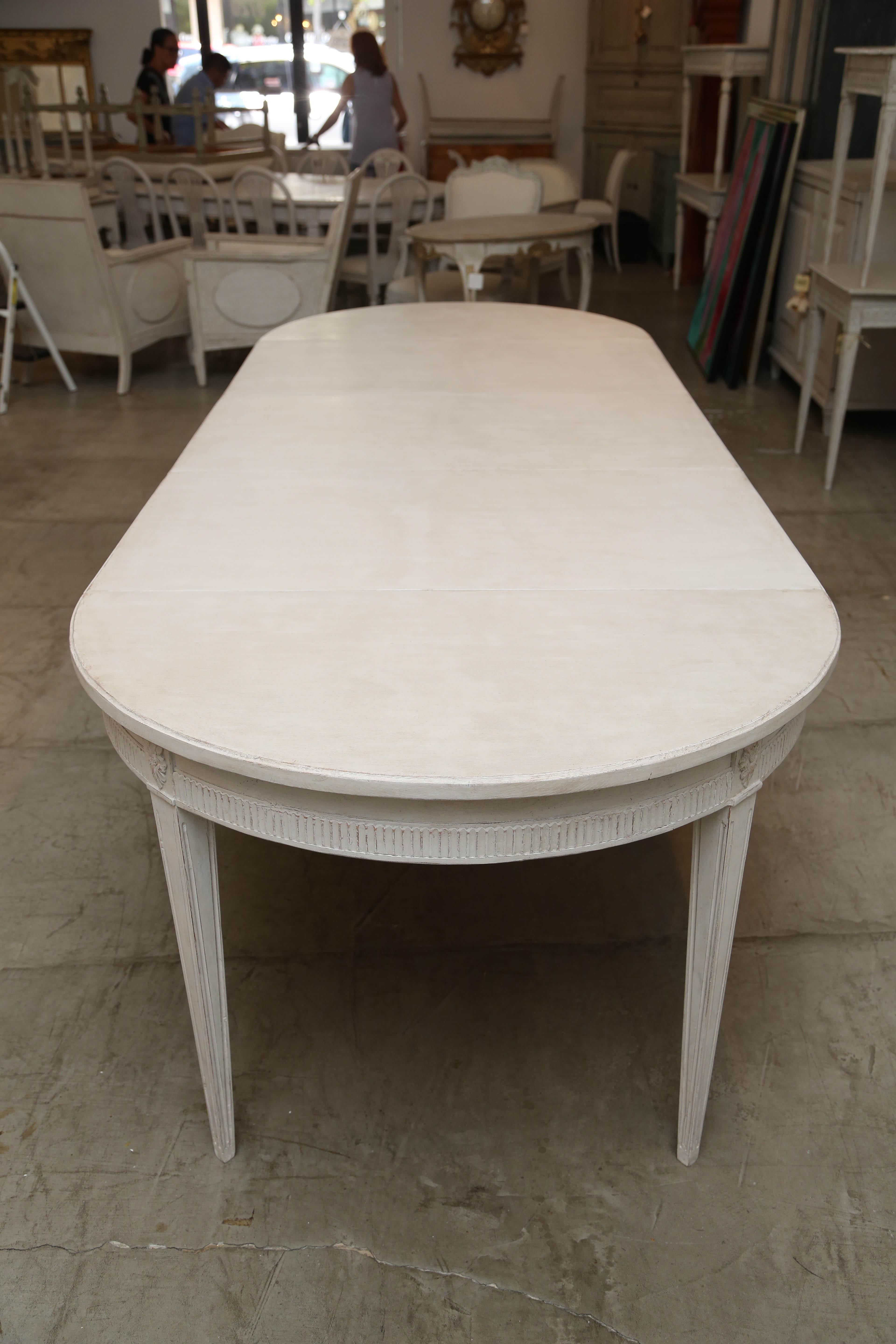 Antique Swedish dining table with three leaves of later date. Painted a distressed Swedish white with grayish highlight finish, has four tapered fluted legs and one center support leg. Carved rosette on the top of each leg. The table is very sturdy
