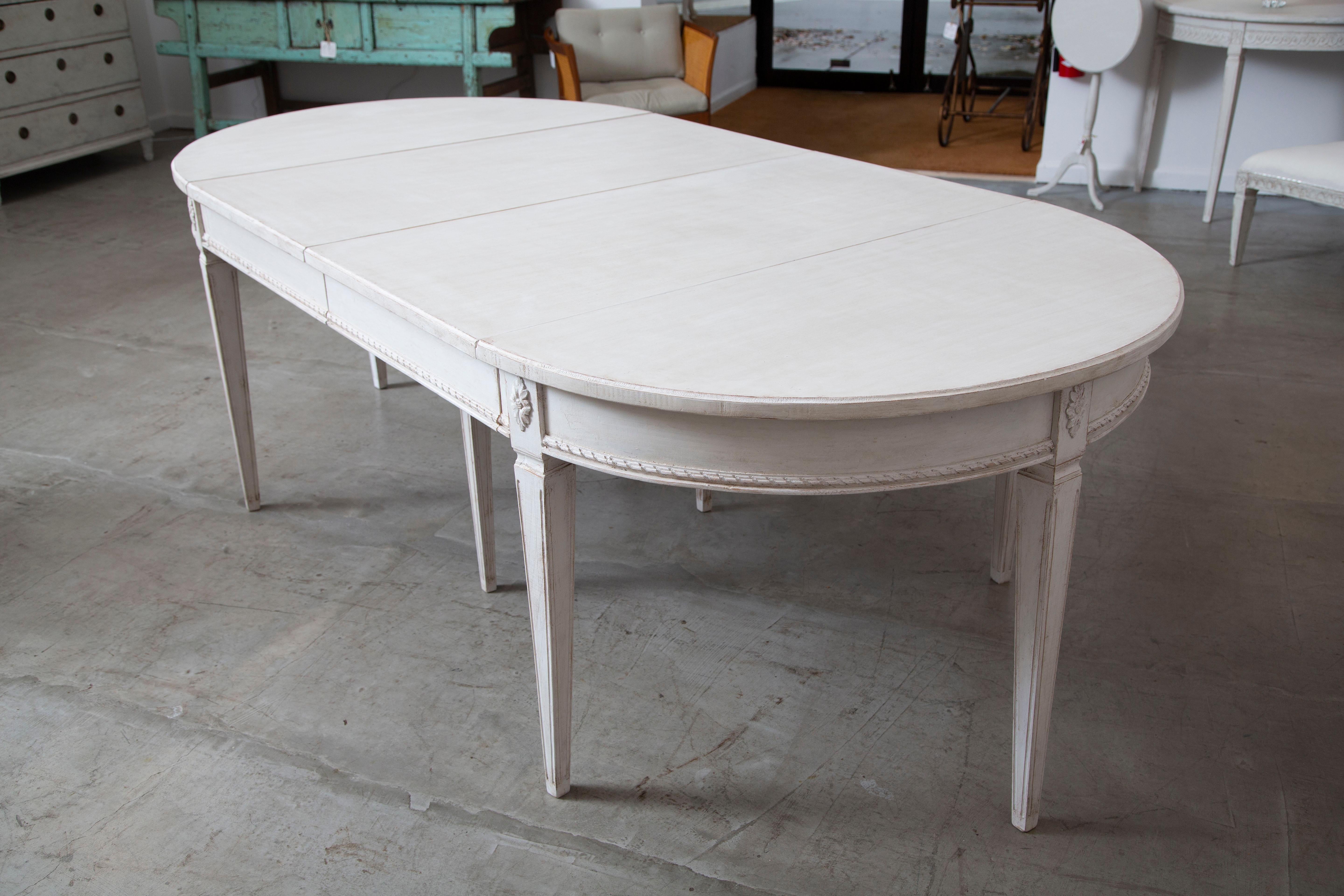 Antique Swedish Gustavian style extension dining table with four leaves, painted in distressed Swedish
creamy white finish, has a lovely patina. Six square tapered fluted legs and one centre support leg. Oval carved rosettes mounted at top of each