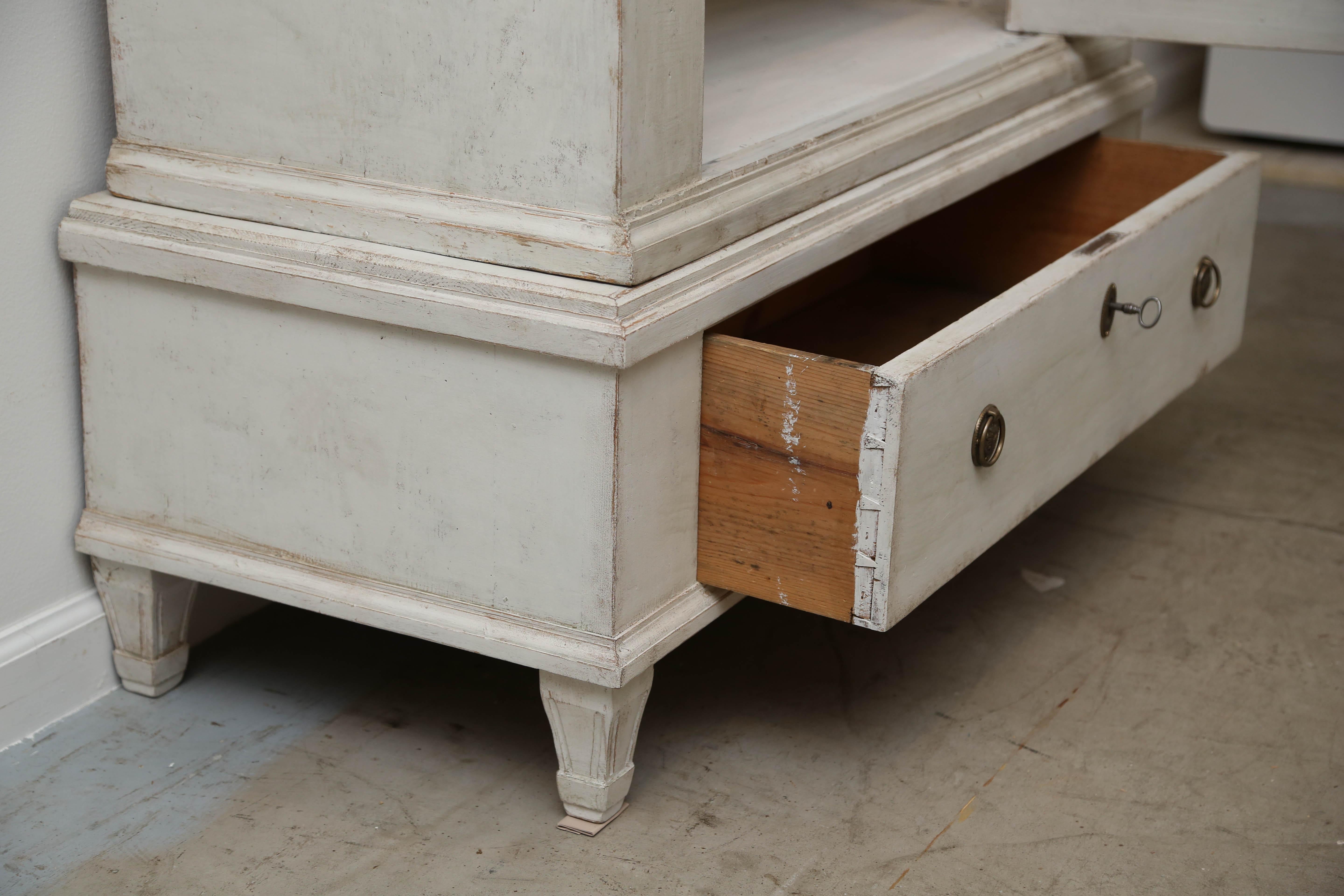 Antique Swedish Gustavian style cabinet painted distressed Swedish white color. Lovely carved crown molding. One raised panel original glass door with lock and key. Cabinet sits on a raised base with fluted legs and one drawer that includes it's own