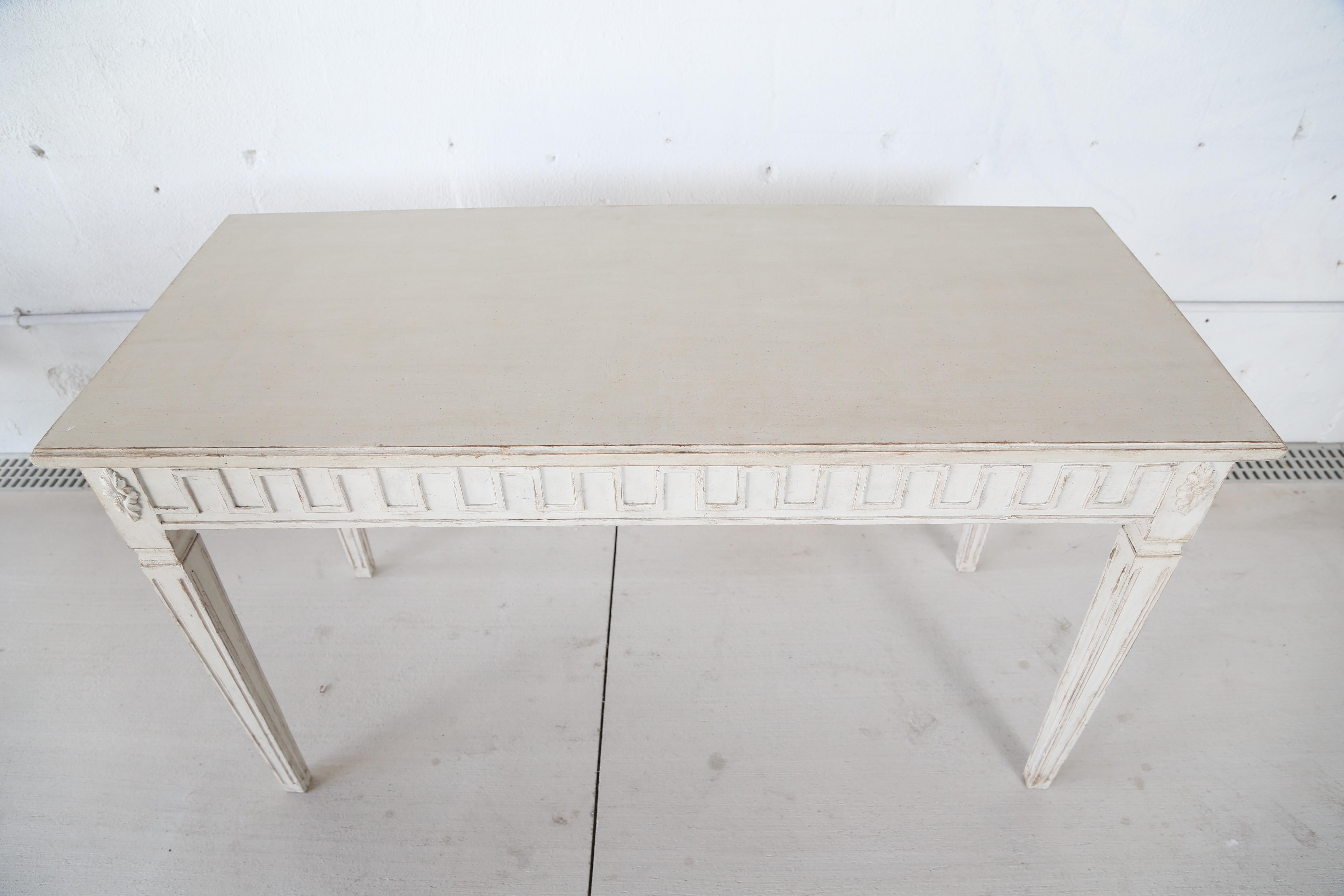 Antique Swedish Gustavian style painted console in Swedish white, apron adorned with Greek key carving and rosettes on the corners, square tapering fluted legs, simple white top, late 19th century.
 
Measures: H 30.75