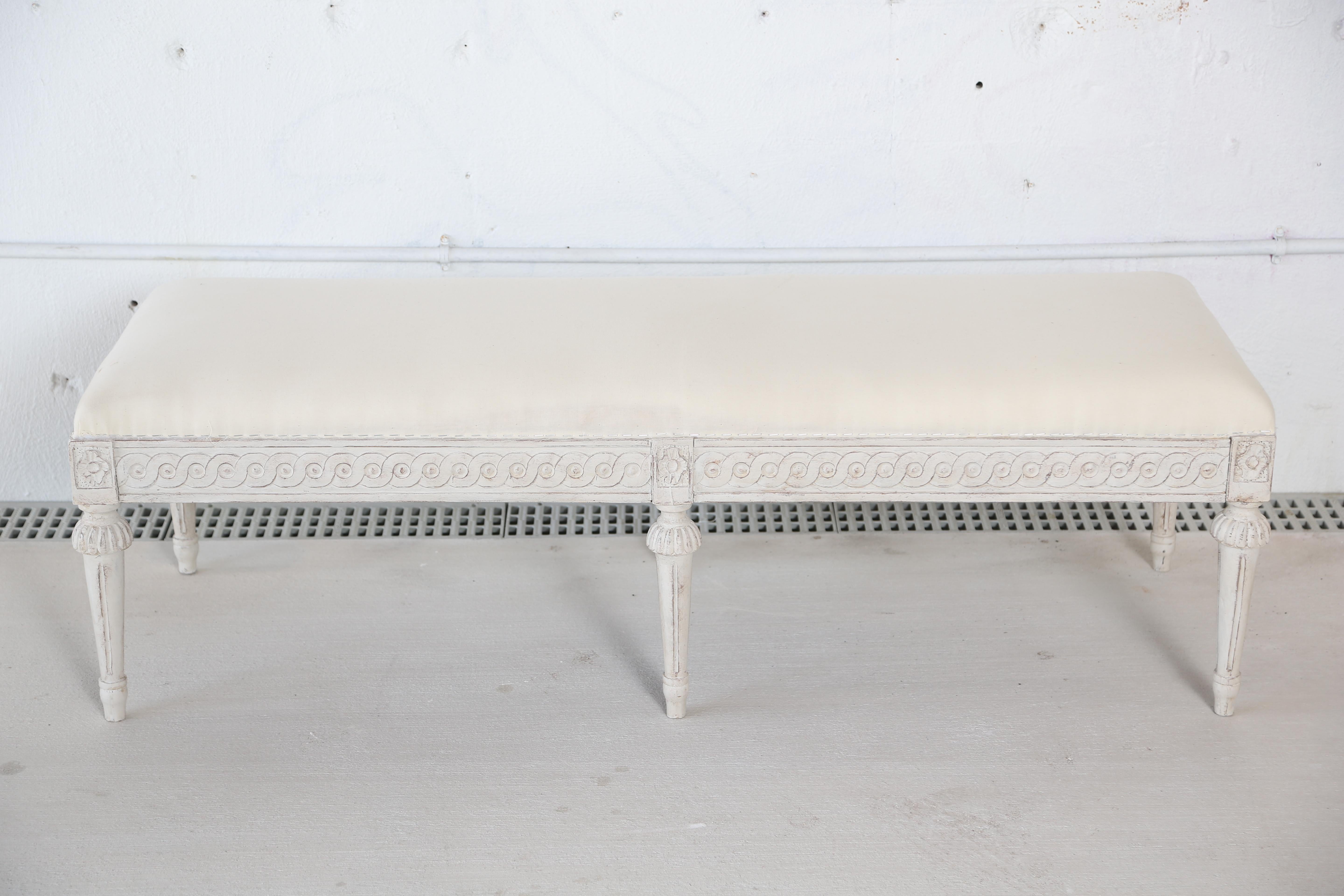 Antique Swedish Gustavian style painted six-leg bench antique Swedish style white painted six-leg bench with upholstered top.
Lovely circular carved border below the seat and a carved rosette above each leg.
Tapered fluted legs with a leaf carved
