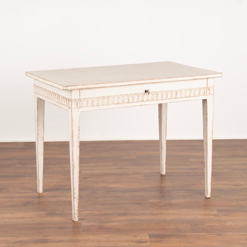 Swedish Gustavian style side table with tapered legs. Scalloped carved details surround the skirt, including long single drawer.
Interior of drawer in sections, refer to photos. 
Restored, later conservator painted in shades of white. 
Sweden circa