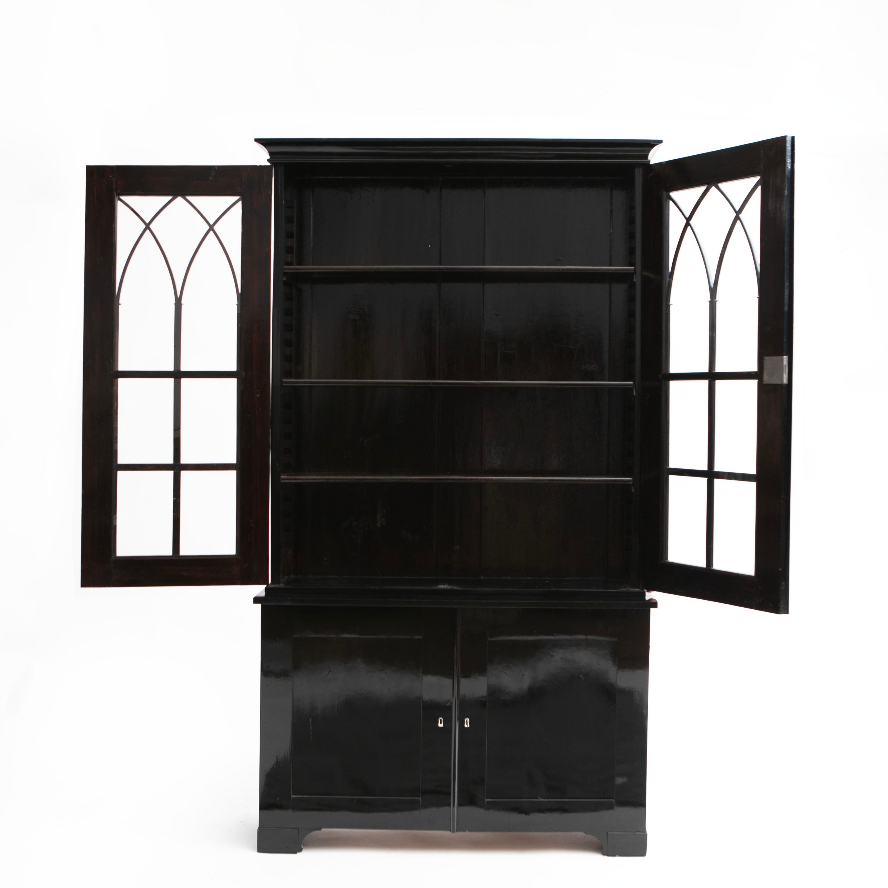 Swedish late empire bookcase / display cabinet in black-polished birch.
In 2 parts, upper case having mullioned glass front with cathedral arch cornice. 
Lower part with a pair of paneled doors. Both opening to shelved interior.
(Cabinet is in two