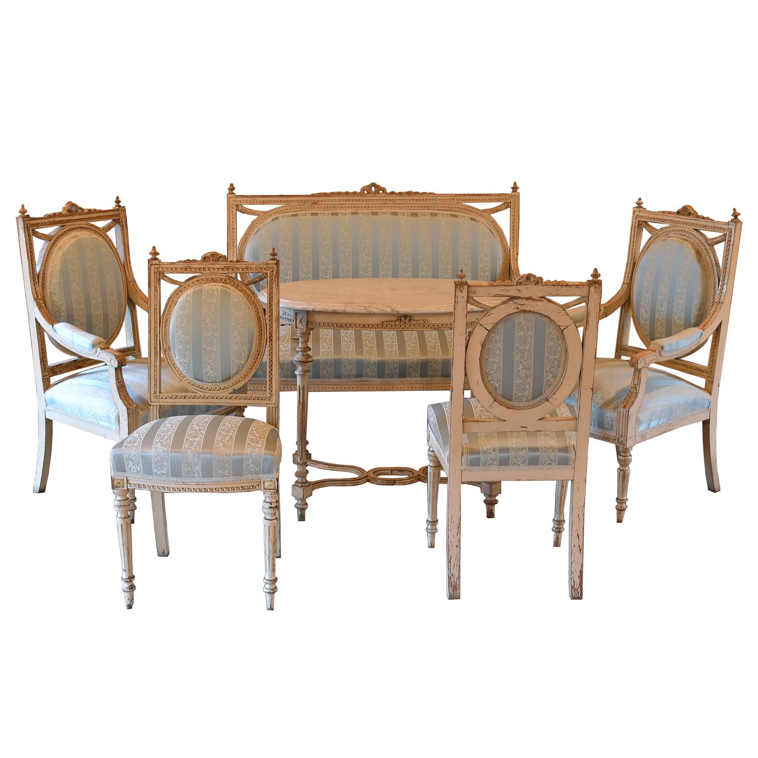 A lovely Louis XVI style salon suite comprising of: (1) canape or settee, (2) armchairs, (2) side chairs & an oval tea table. Sweden, circa 1915. Carved wooden frames have the original white/grey Gustavian paint with just the right amount of