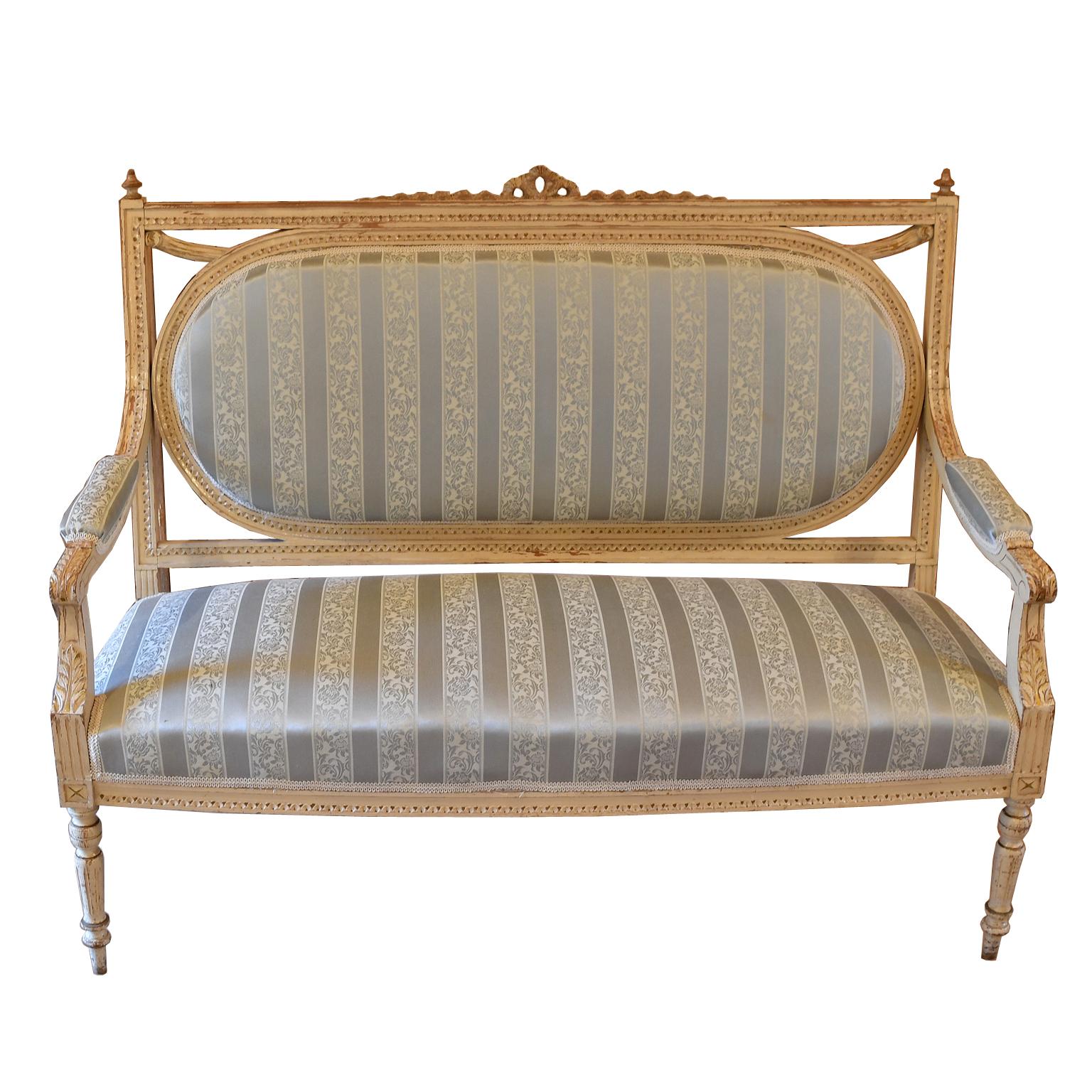 A lovely Louis XVI style canape/ settee with upholstered seat & back, & painted white/grey distressed finish on wooden frame. Details include carved swag & acanthus-leaf motif, with turned front legs & saber rear legs. While more recent but not new,