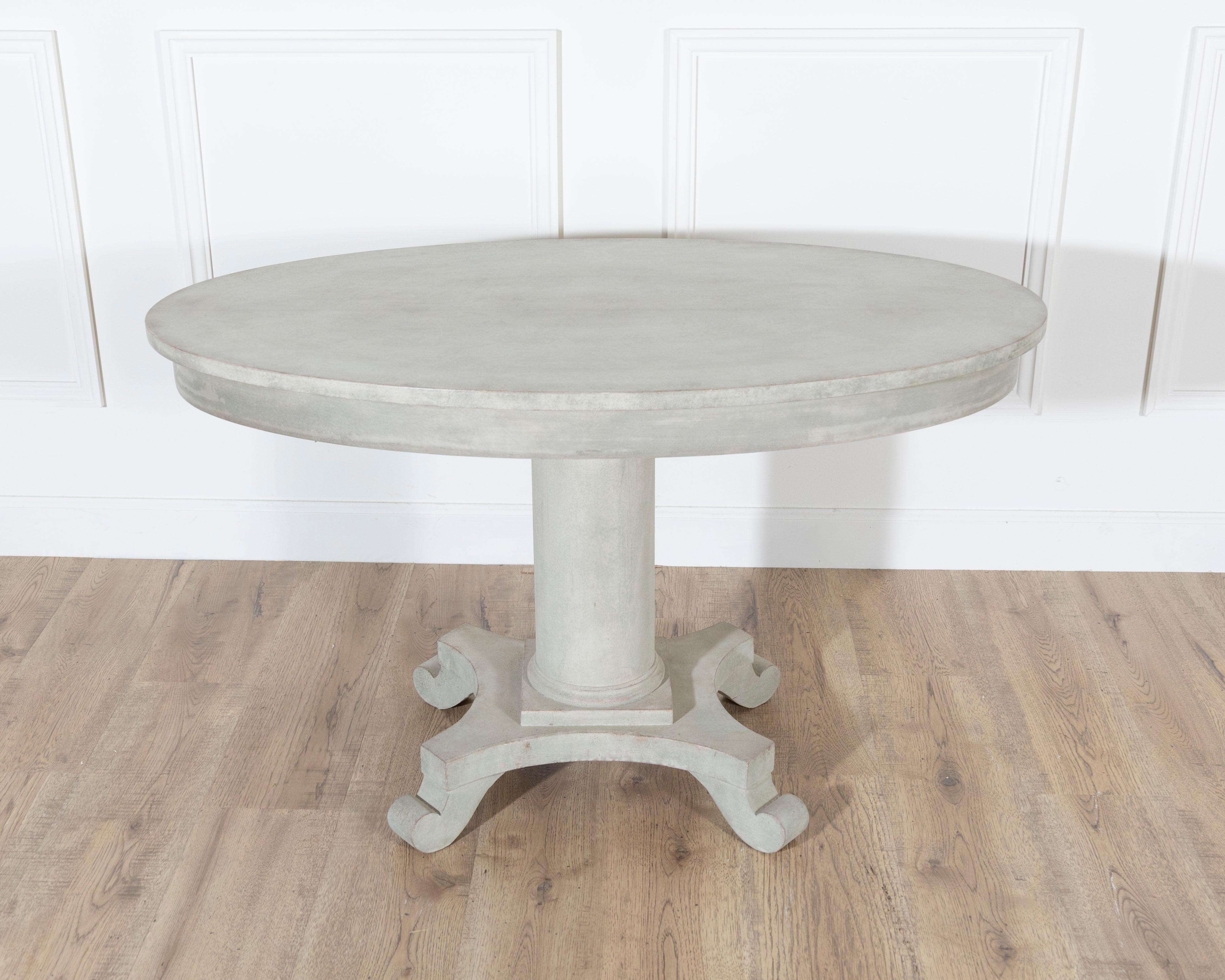 A Swedish oval center table from the early 20th century, circa 1900–1910, painted in a soft blend of green and grey that has aged into a fine patina. The oval top is supported by a single column resting on a sturdy four-armed base, each foot shaped