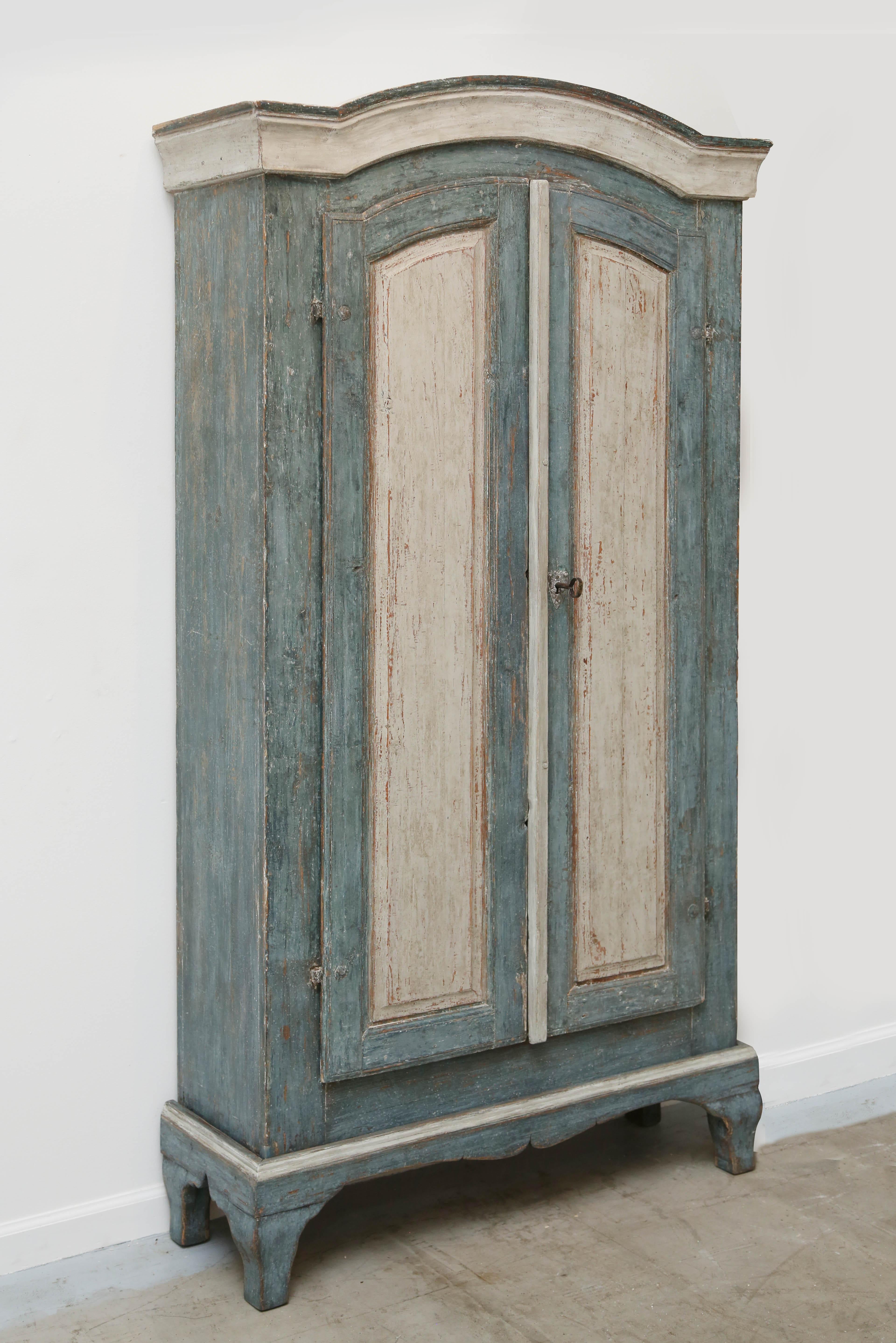 Antique Swedish Baroque distressed original painted blue and white- greyish armoire /cabinet. Lovely carved arched wood top cornice. Two full length raised panel carved doors with original lock and key. Cabinet sits on a raised base with curved legs