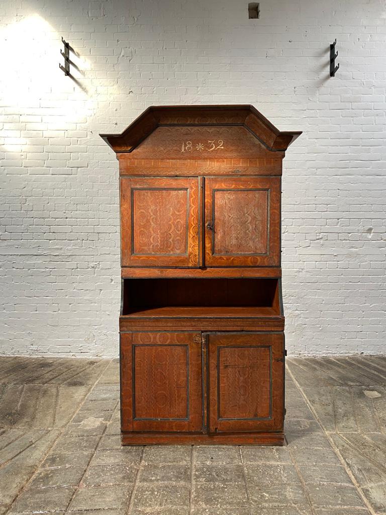 An antique Swedish Baroque taste cabinet with the most beautiful combed paint decor. The colour is mellow and natural red colour.
The cabinet features a Swedish crown pediment with the painted date of date 1832. Underneath this, a pair of cupboard