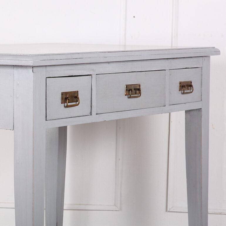An early-20th century Swedish painted three-drawer writing table or desk, the painted top with molded edge above a frieze fitted with three drawers with hand-cut dovetail joinery and original brass pulls, the whole standing on square tapering legs.