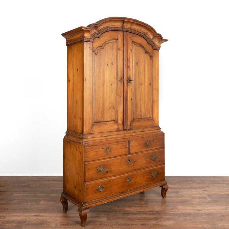The gentle beauty of this Swedish cupboard is found in the deep patina of the aged pine, dated to the early 1800's (notice the original hinges and wood pegs used for nails).Carving along the curved bonnet and panel doors adds depth and character,