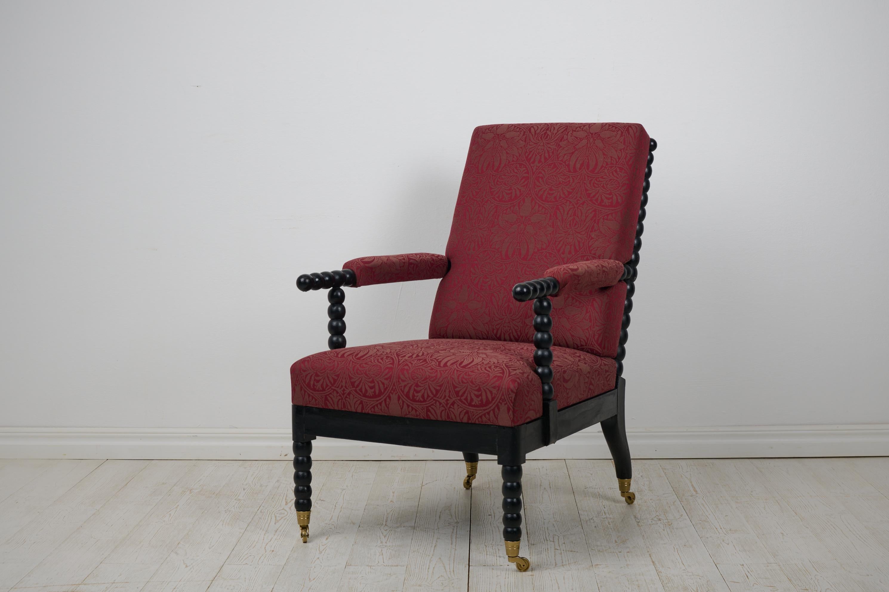 Ancienne chaise à fuseau ou chaise longue suédoise du milieu des années 1800. La chaise est confortable et généreuse avec un cadre en bois noirci et une assise, un dossier et des accoudoirs rembourrés. Modèle inhabituel avec un cadre fait de sphères