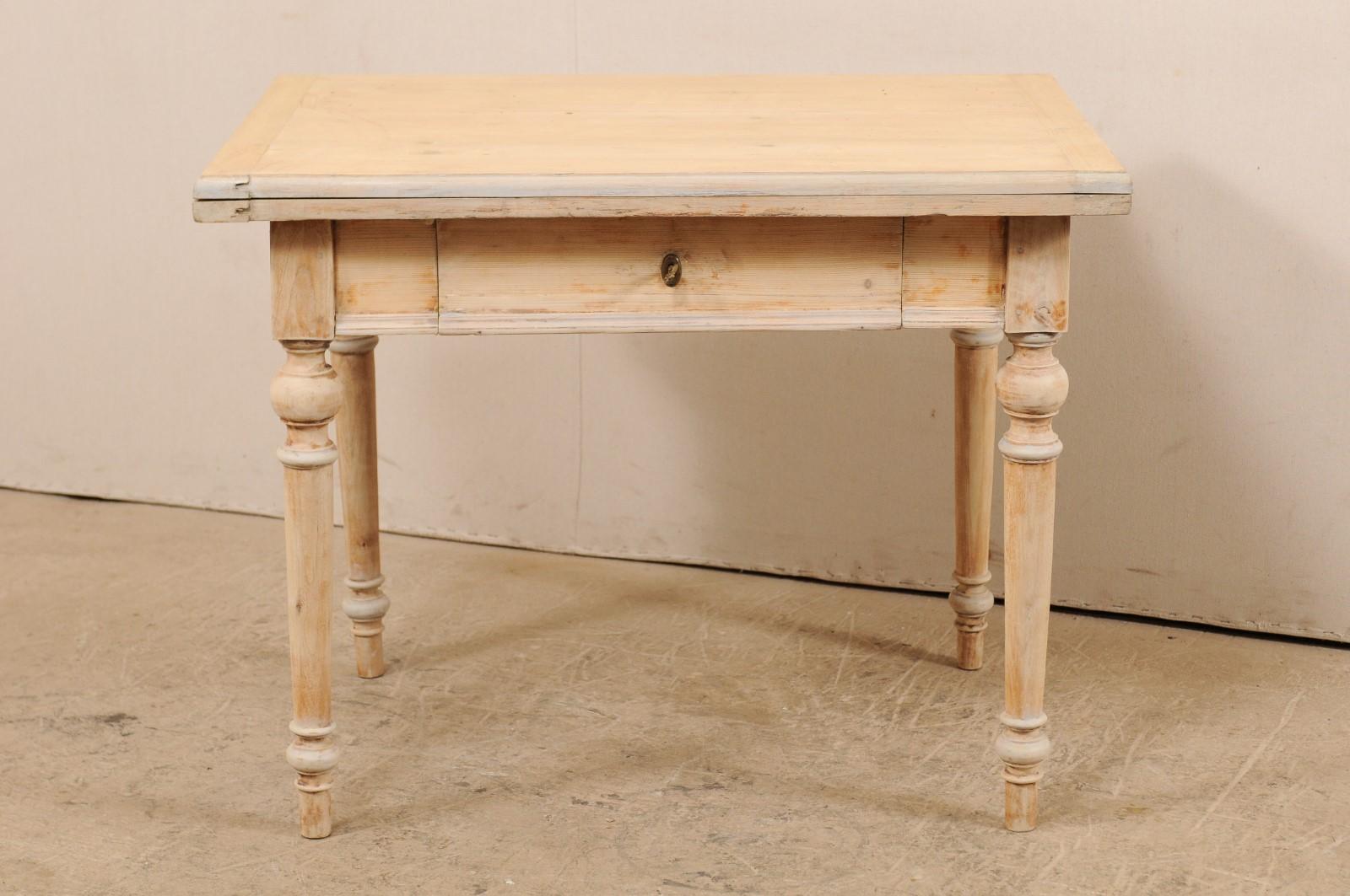 A Swedish bleached wood table with transitional or fold out top from the early 20th century. This antique table from Sweden features a top that doubles, over a clean skirt that houses a single drawer, and raised upon four nicely turned legs. When