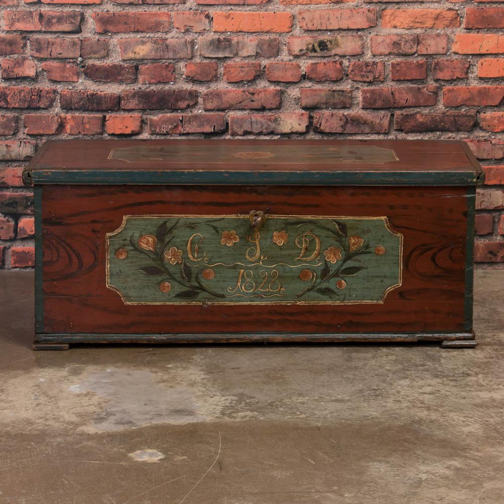 Exceptional pine blanket chest from Sweden dated 1828 with the original rust colored faux wood grain paint and a satin wax finish. There are stunning painted panels on the front and top - both with floral branches on a light blue colored background.