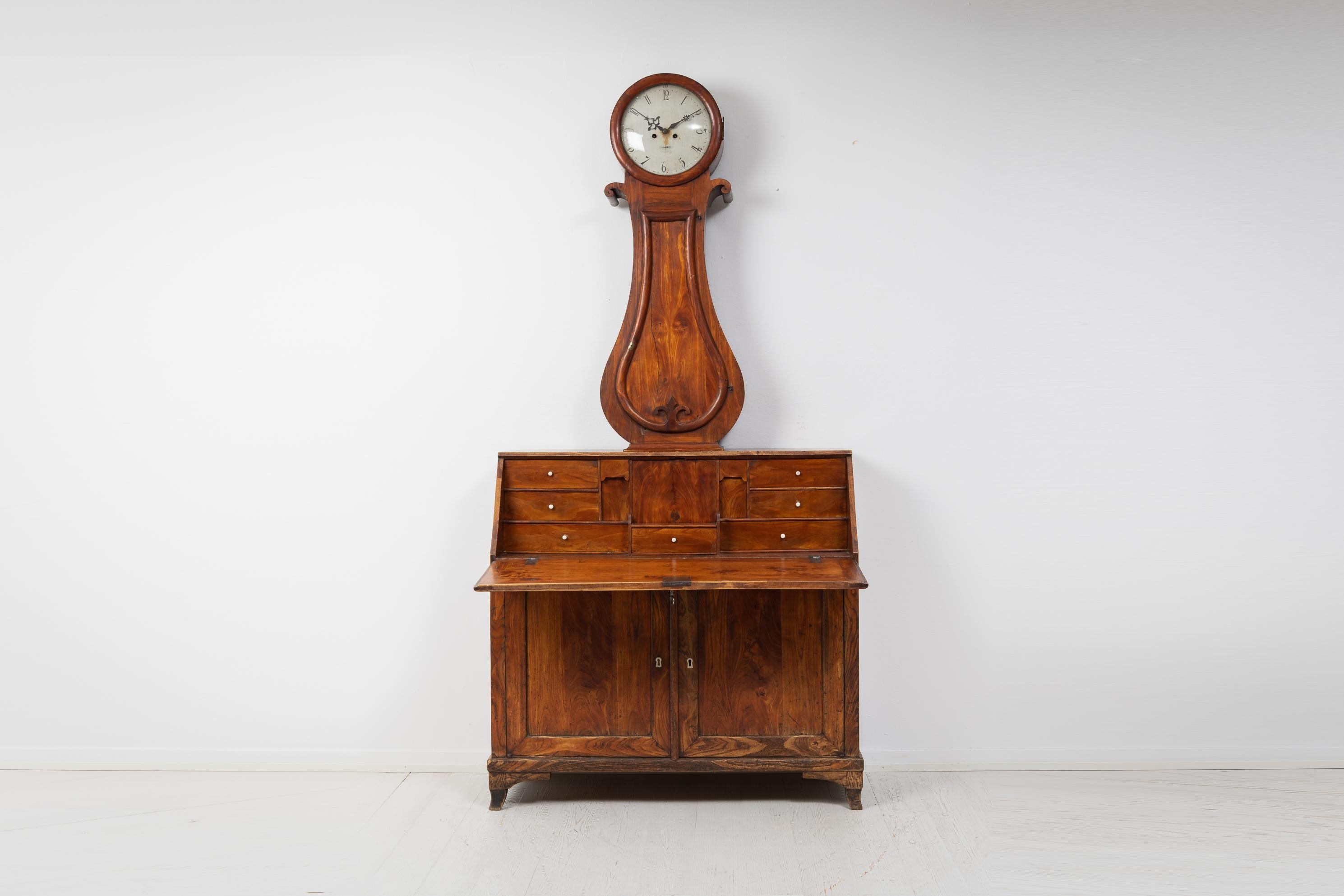 Swedish antique clock cabinet made during the early to mid 1800s, circa 1820 to 1840. The cabinet is veneered and waxed elm. The lower cabinet is a secretary desk and the upper consists of a long case clock. The cabinet has hardware and drawer pulls